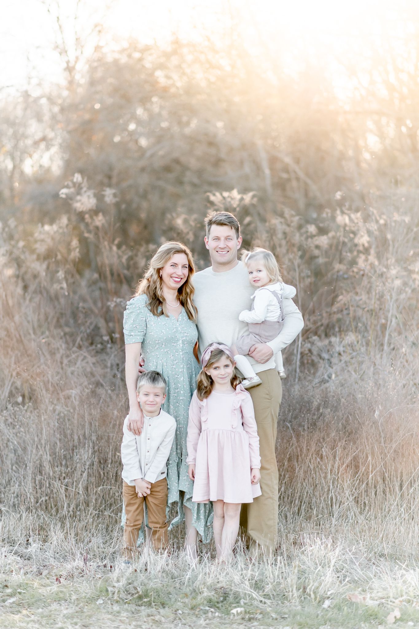 Family of 5 smiles as they pose in a field at sunset