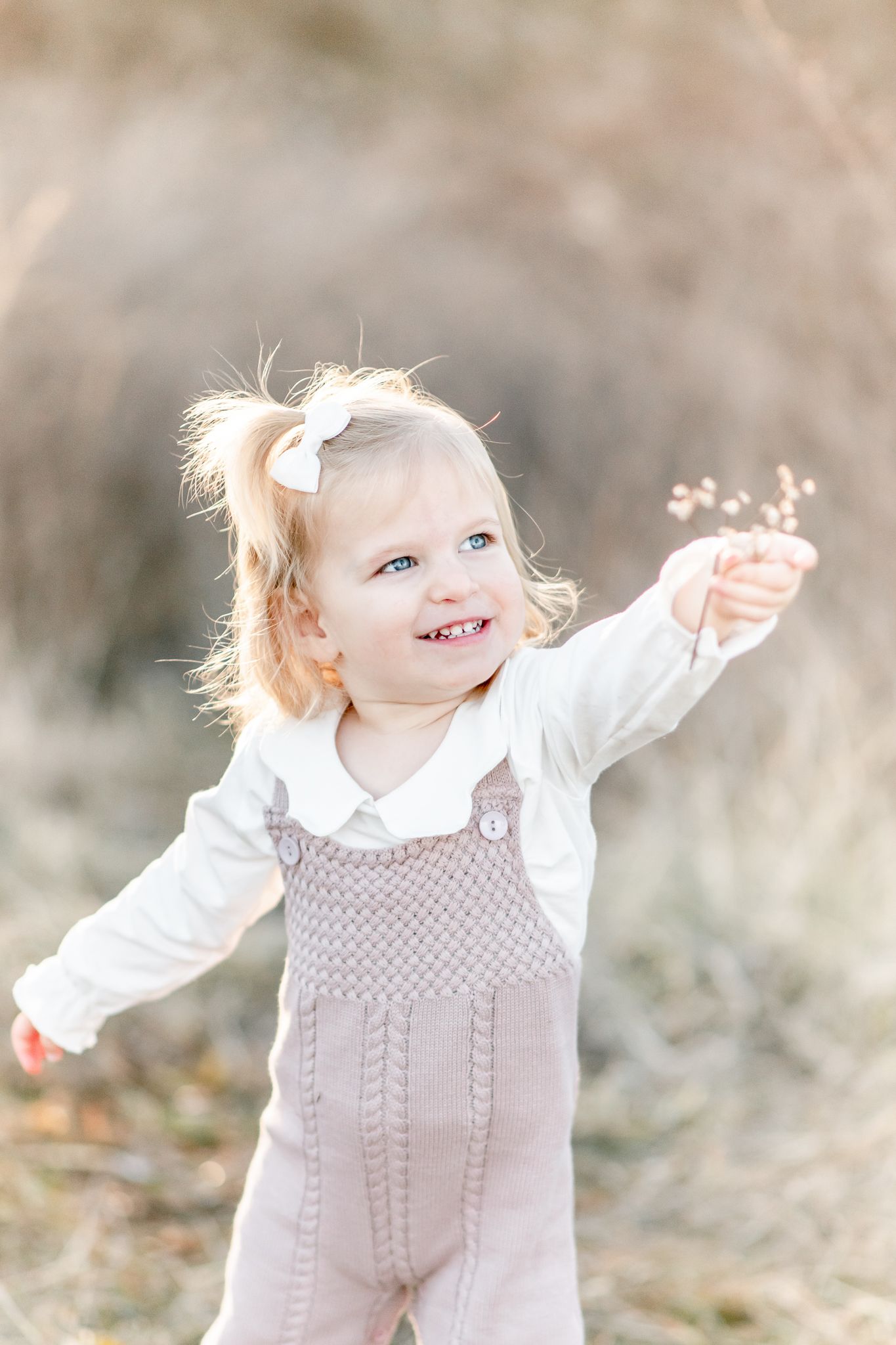 Toddler holds up wildflowers as she smiles up at her mom