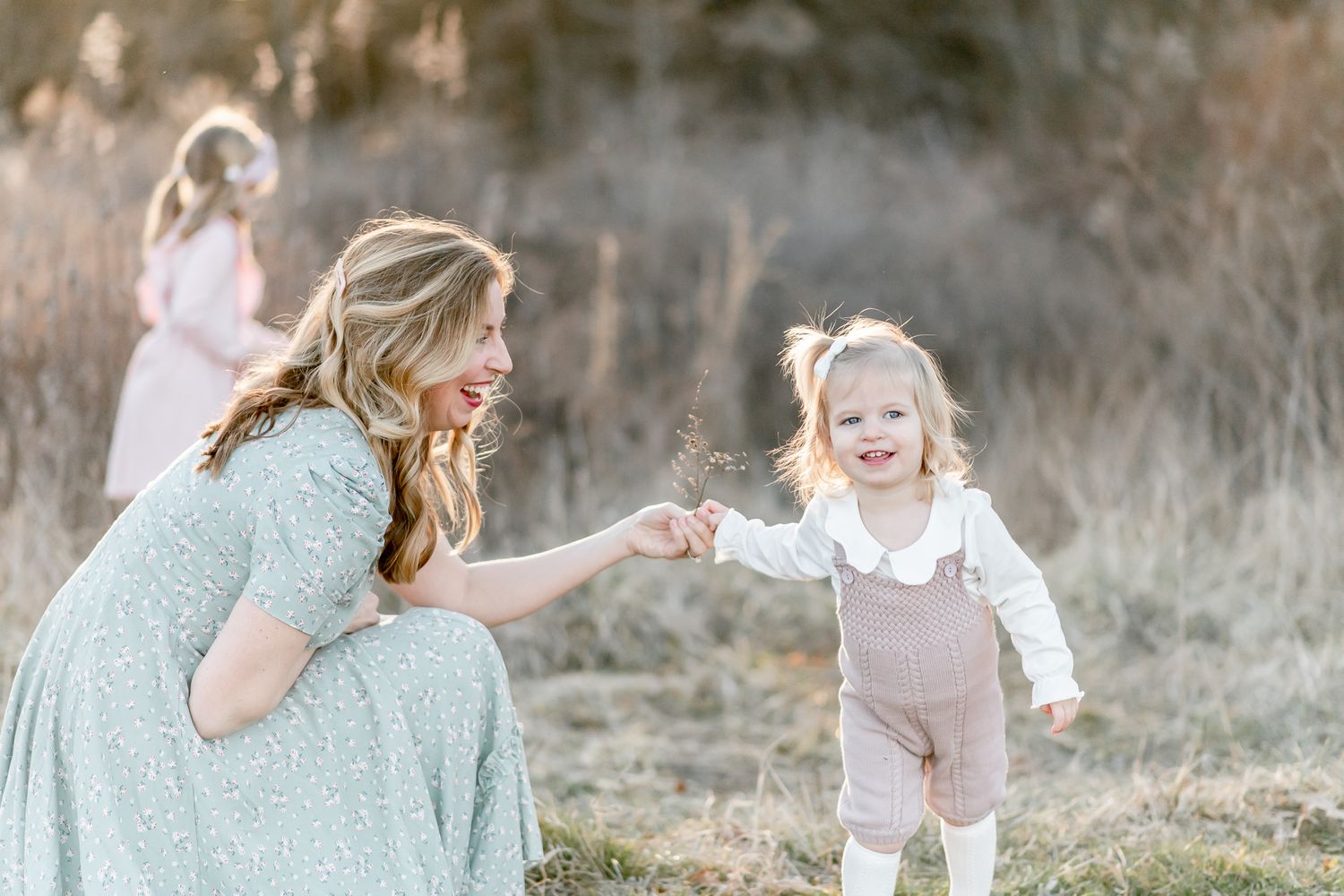 Mother kneels down to take flowers from toddler