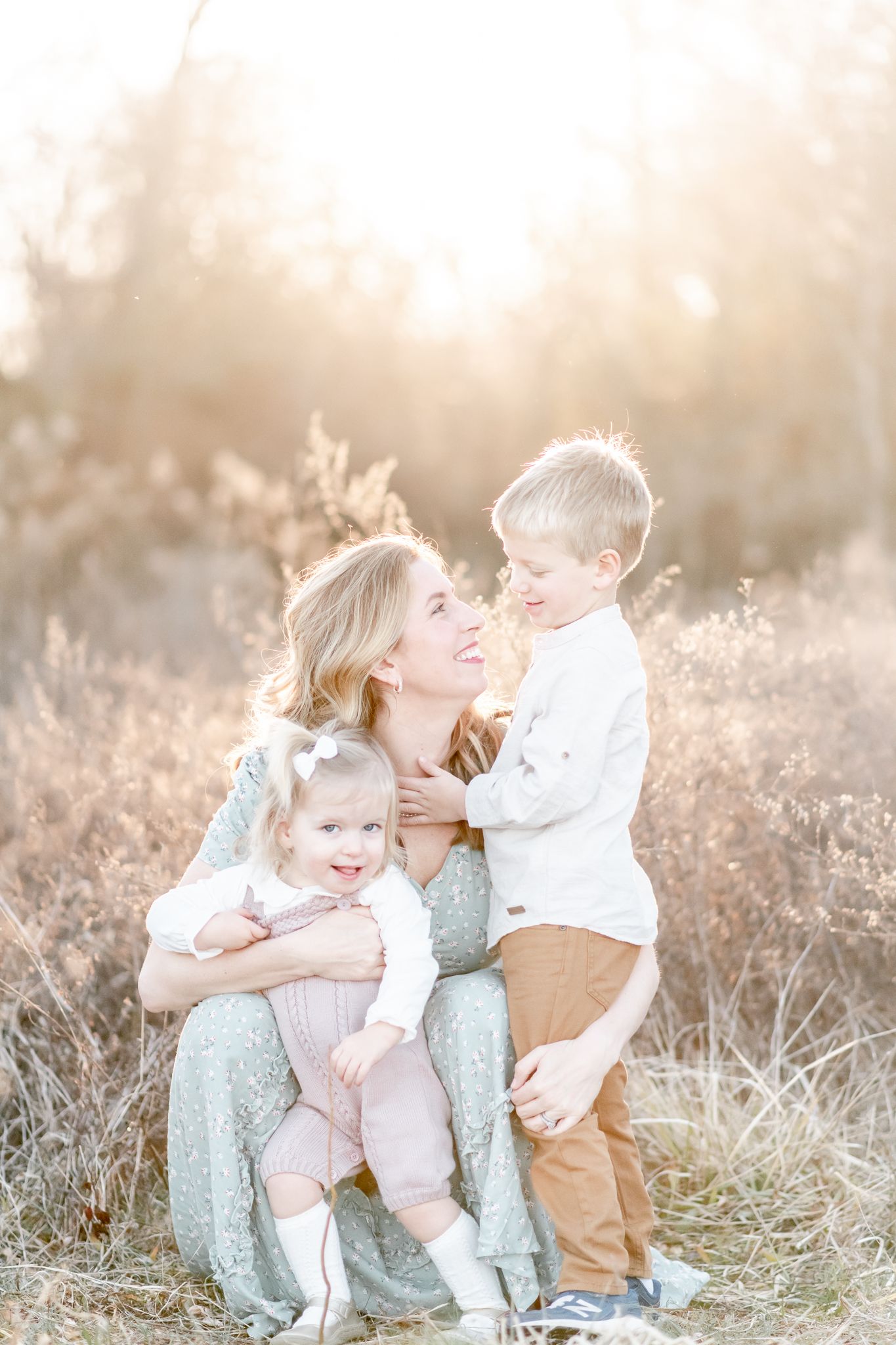 Mother snuggles with her two toddler children in a field