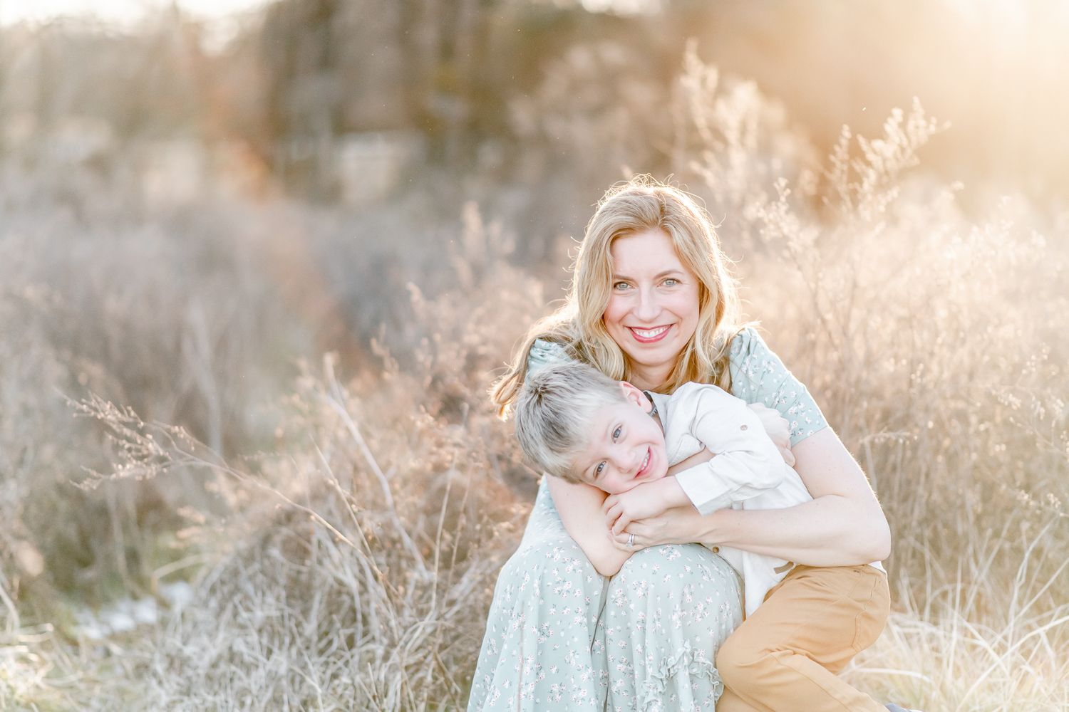 Mother holds her son tight in a field at sunset