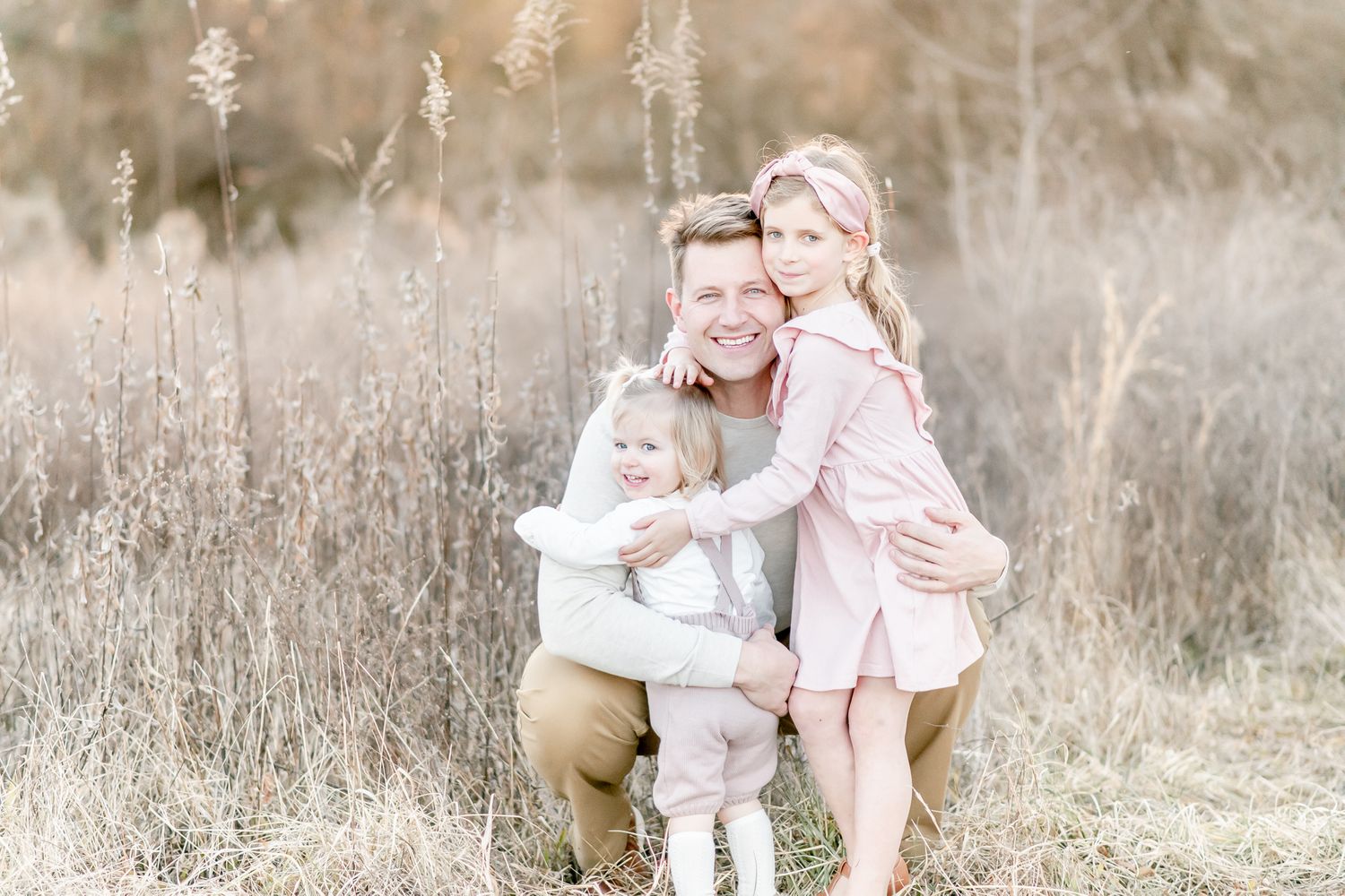 Father snuggles with his two daughters in a golden field