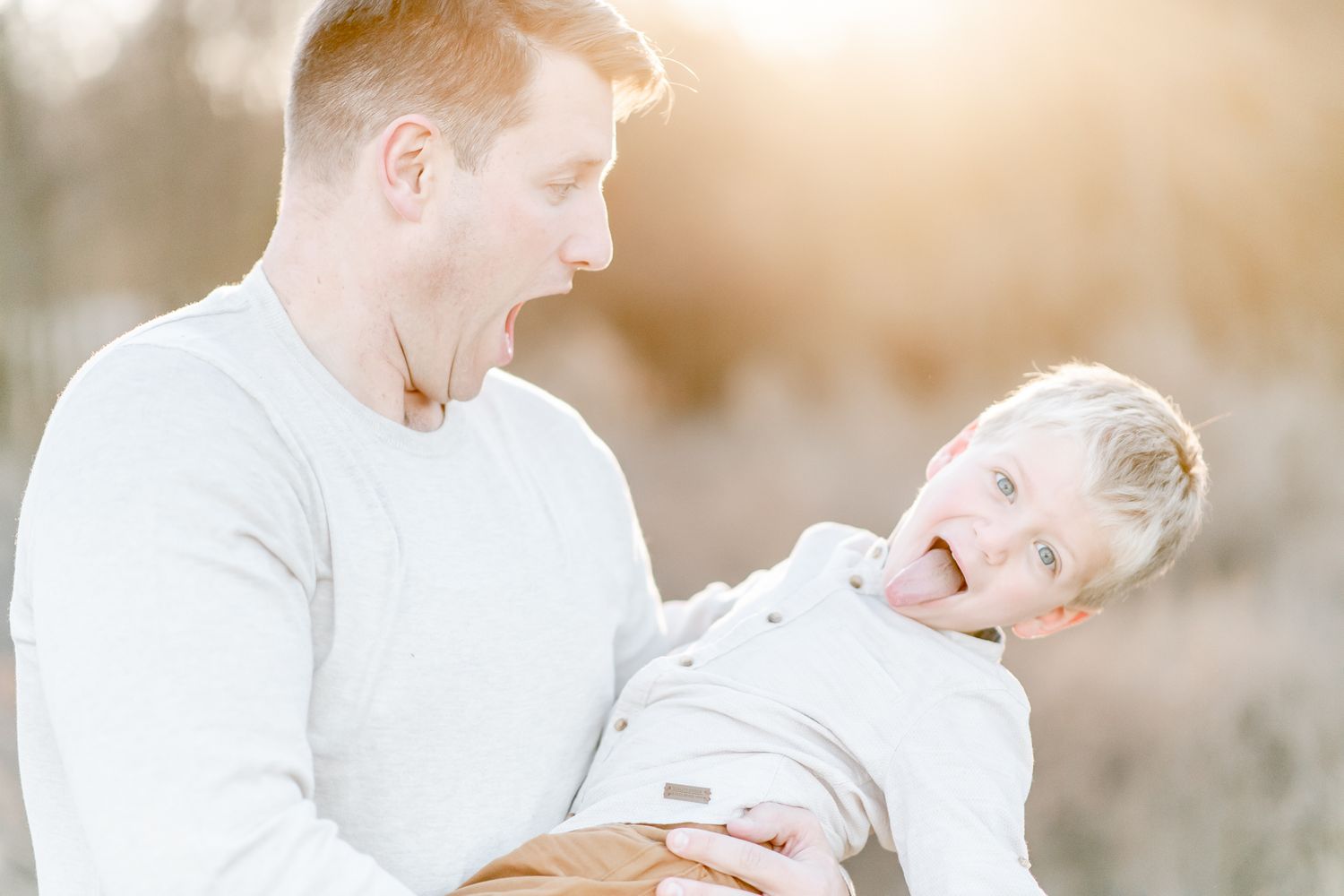 Father holds son as he leans back and sticks out his tongue
