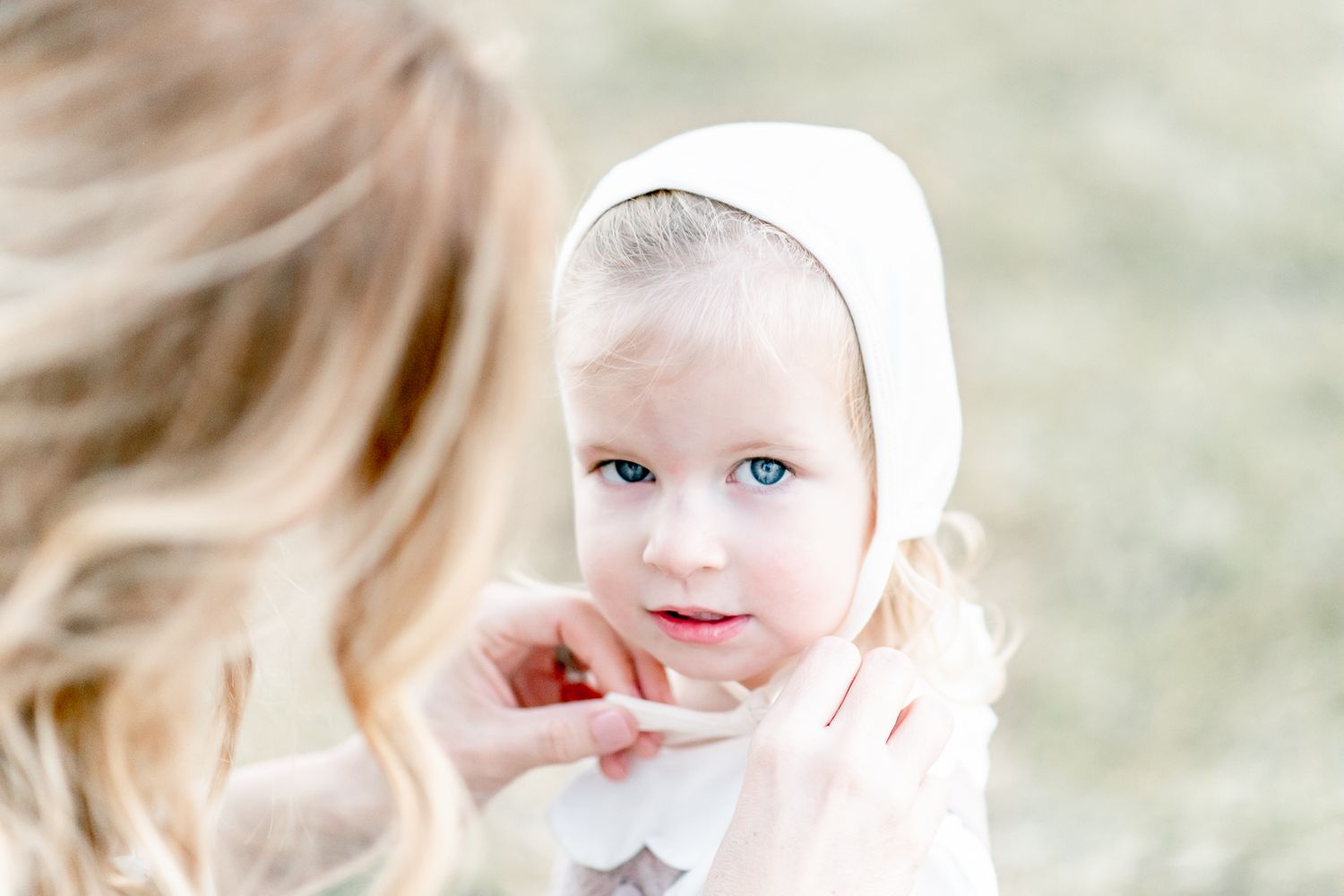 Toddler looks up as her mother ties a bonnet on her head