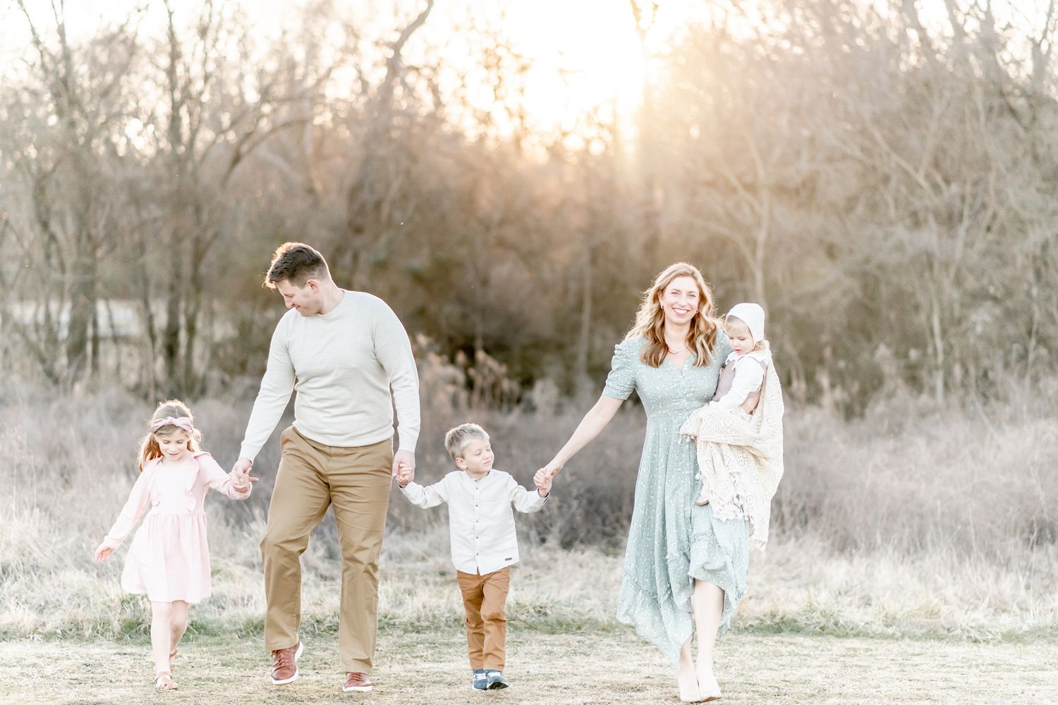 Family of 5 walks holding hands in a field at sunset
