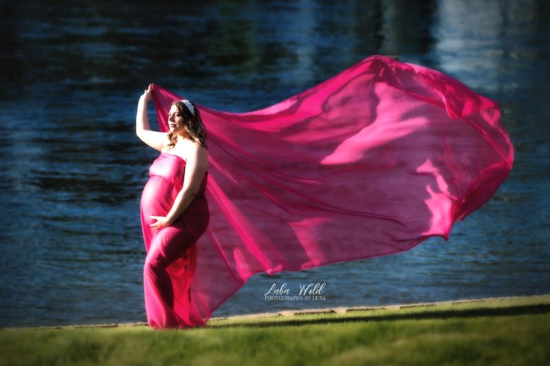maternity pregnant woman in pink flowing fabric by spokane river in coeur d alene Idaho photographer luba wold