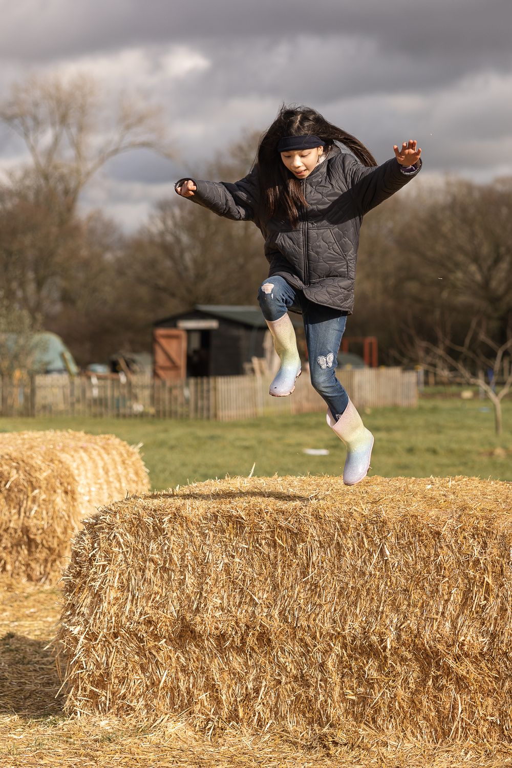 Young girl jumping from hay bales in Aldenham Country Farm