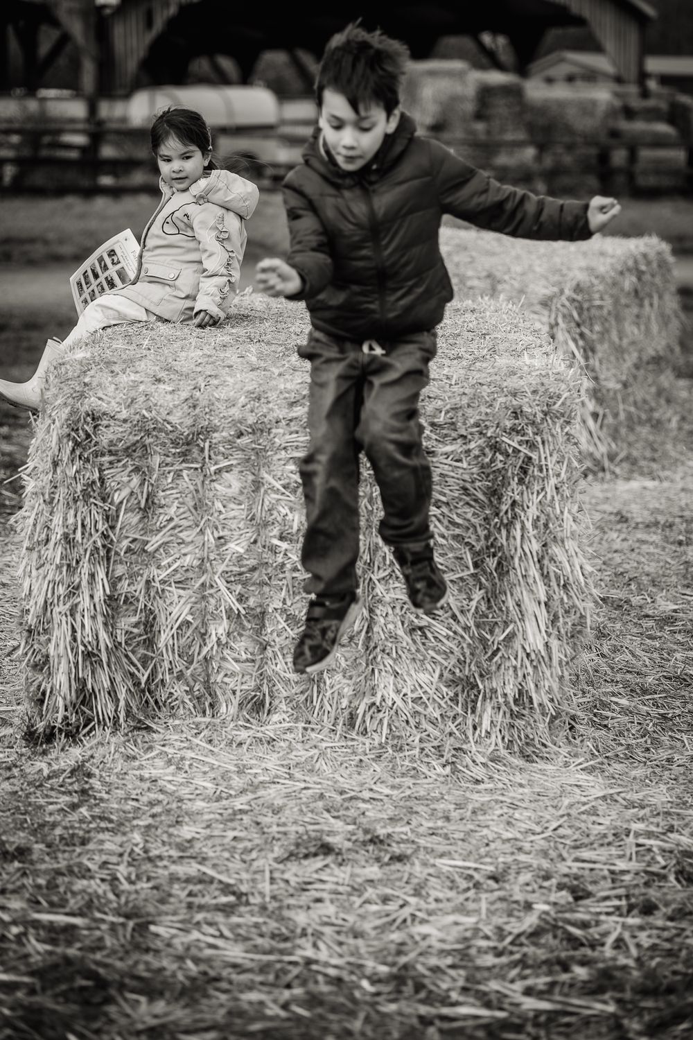 Black and white image of young boy jumping from hay bale in Hertfordshire Farm.
