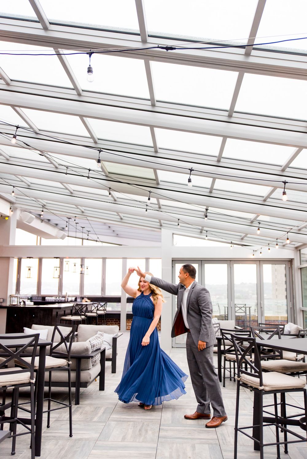 man in grey suit twirling woman in long blue dress on Lytle Park Hotel rooftop engagement pictures