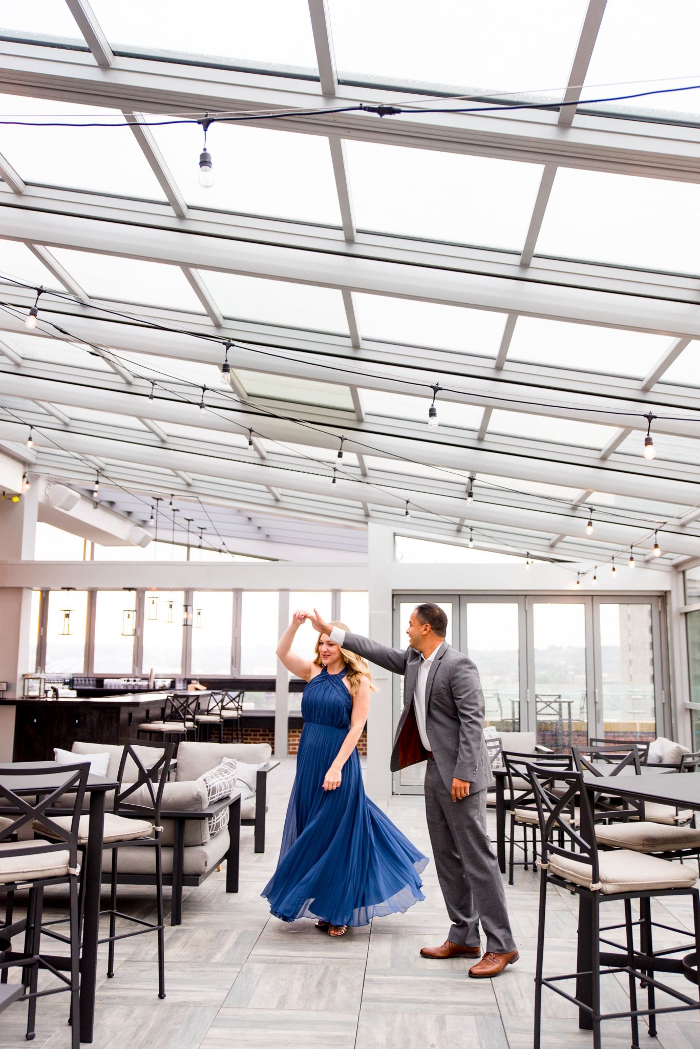 man in grey suit twirling woman in long blue dress on Lytle Park Hotel rooftop engagement pictures