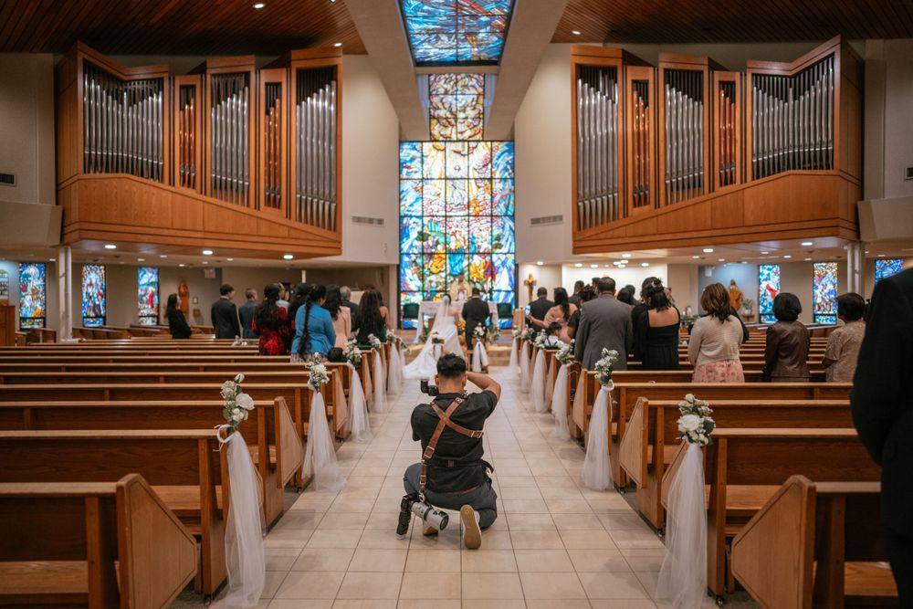 A church interior with wooden pews, stained glass windows, and dual pipe organs during a gathering of attendees.