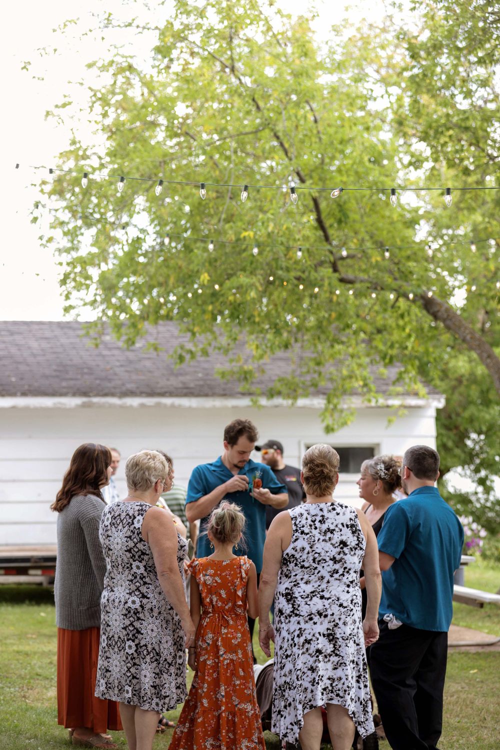 A group gathers outdoors under green trees during what appears to be a social event or celebration.