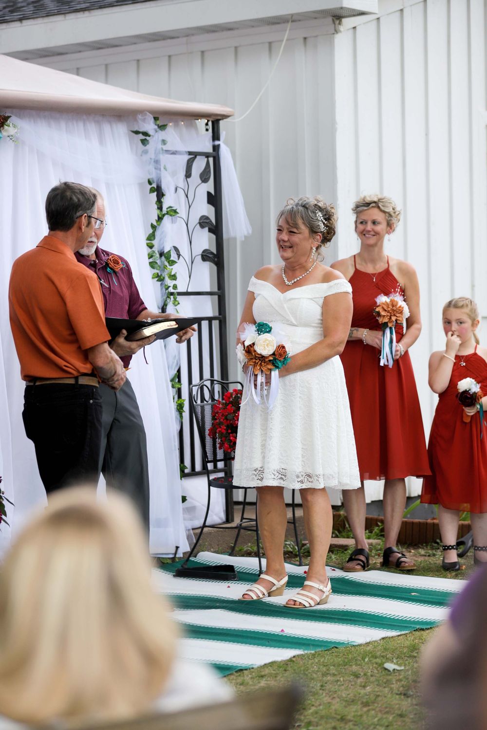 Outdoor wedding ceremony with red and white color scheme featuring attendants in red dresses at a gazebo.
