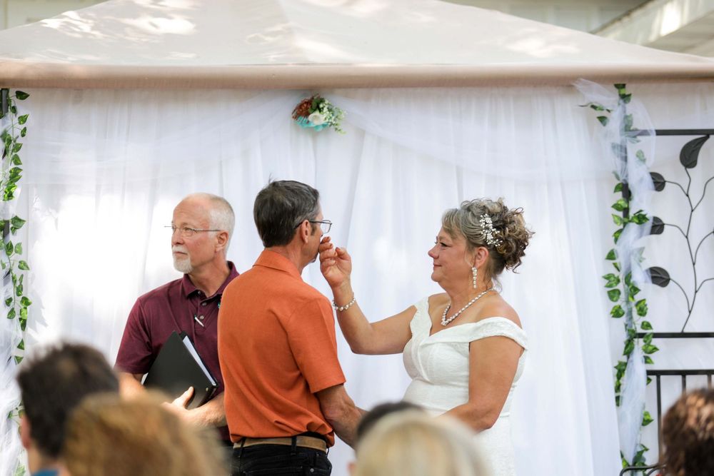 A wedding celebration takes place in a tent decorated with white draping and green ivy garlands.
