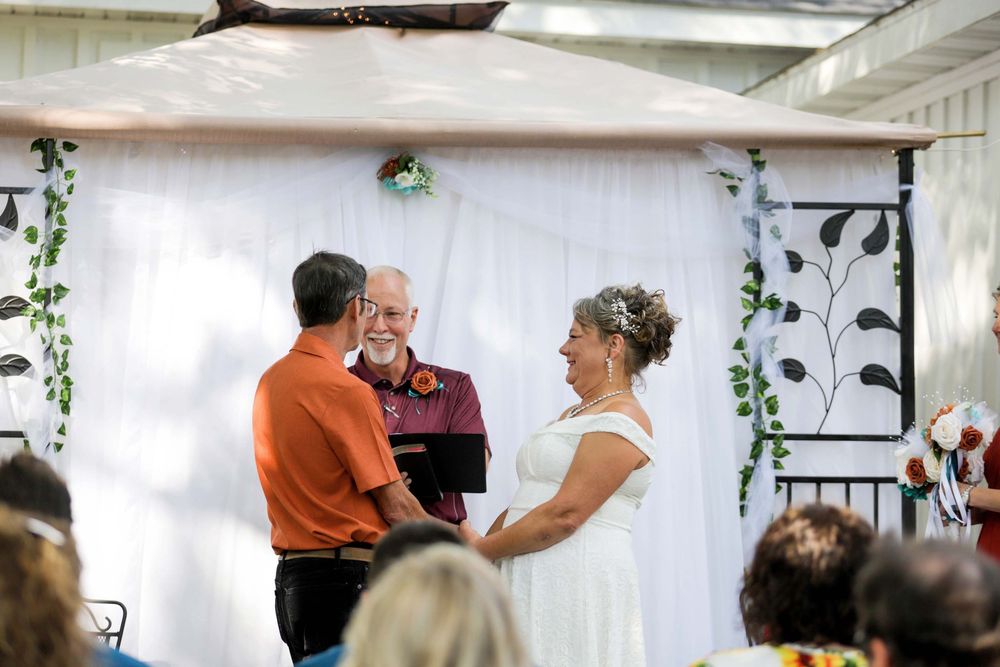 A romantic couple dancing together at an elegant wedding venue decorated with white drapes and hanging greenery.
