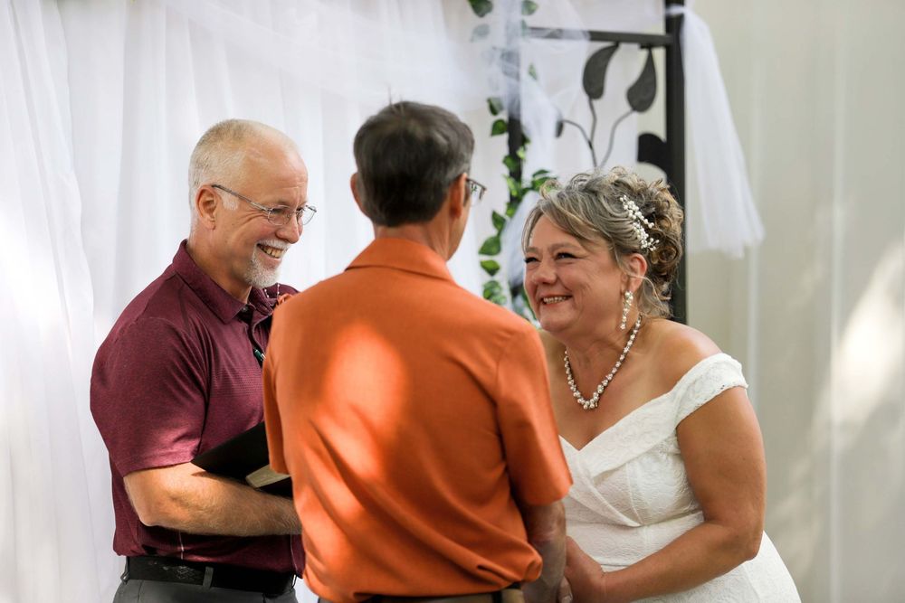 Three people share a joyful moment together at an indoor event space with white curtains in the background.