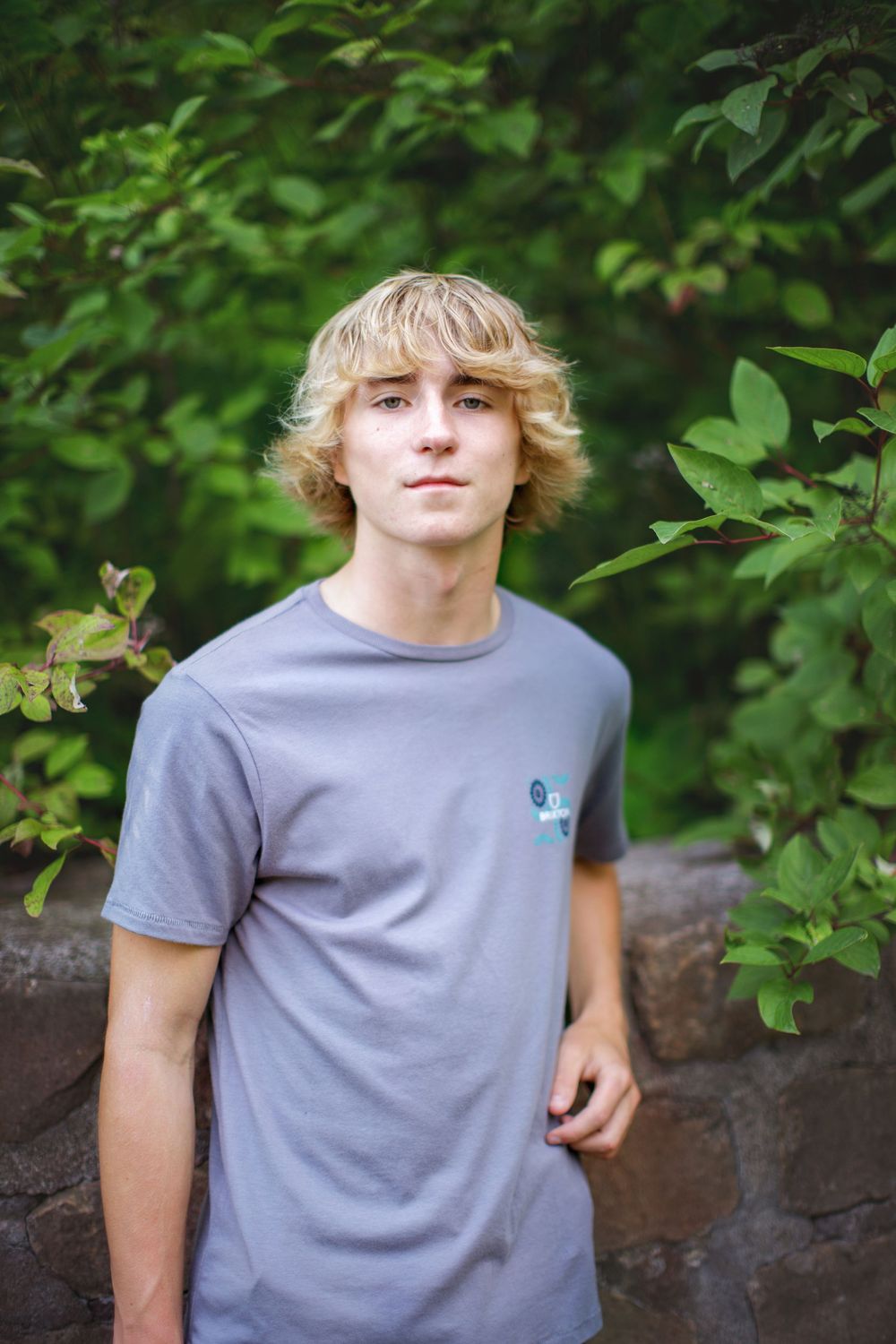 A person in a gray t-shirt stands against a leafy green background in a series of similar casual outdoor portraits.