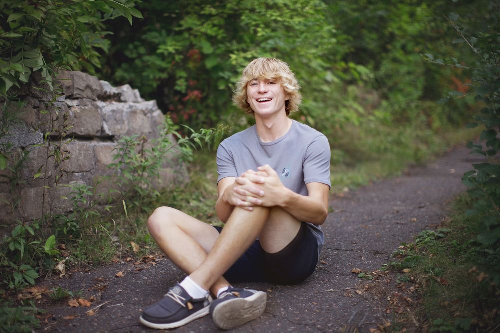 A person in comfortable casual wear sits and reads a book on a tranquil forest trail.