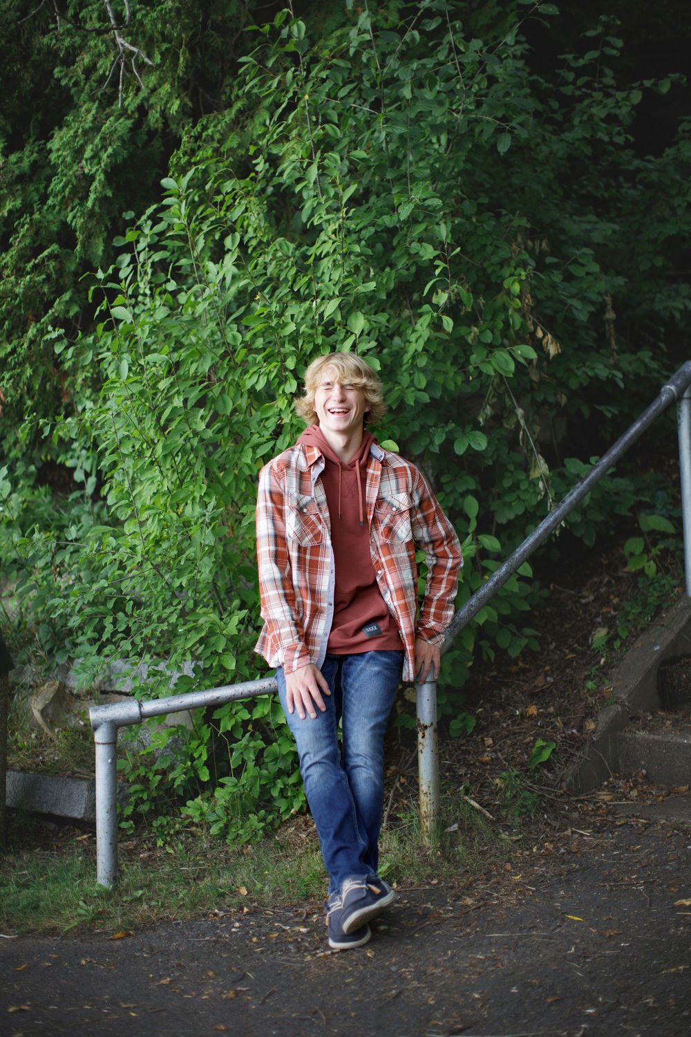 A casual outdoor photo series showing someone in a plaid shirt, jeans and sneakers relaxing playfully in a wooded path setting.