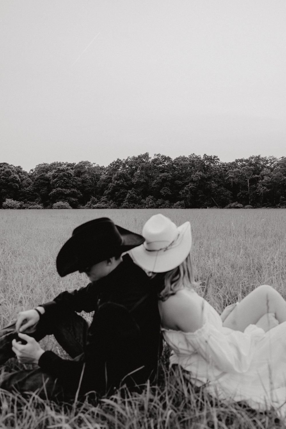 Two people lying down together in a grassy field with trees on the horizon.
