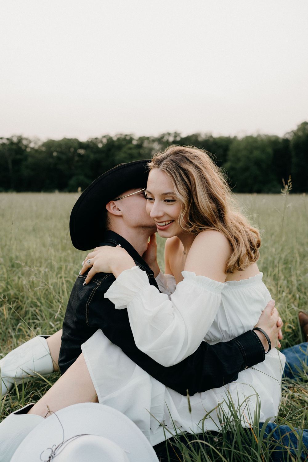 Intimate couple's photoshoot in a rustic field with natural lighting and forest backdrop.