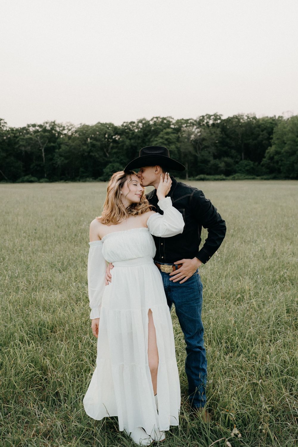 Candid romantic moment captured in an open field with treeline in the background.
