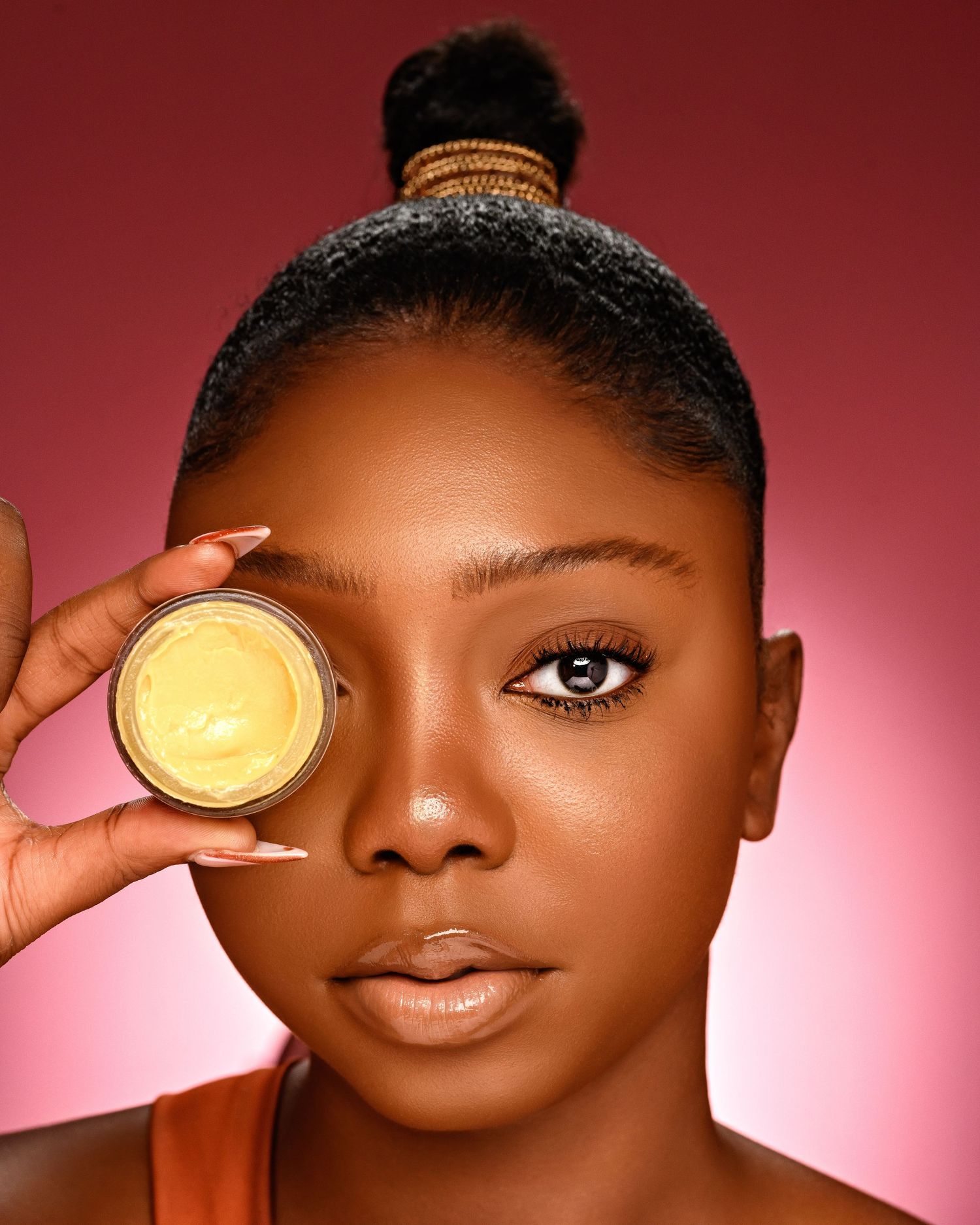 Beauty still life portrait of person holding a golden cosmetic jar against pink background.