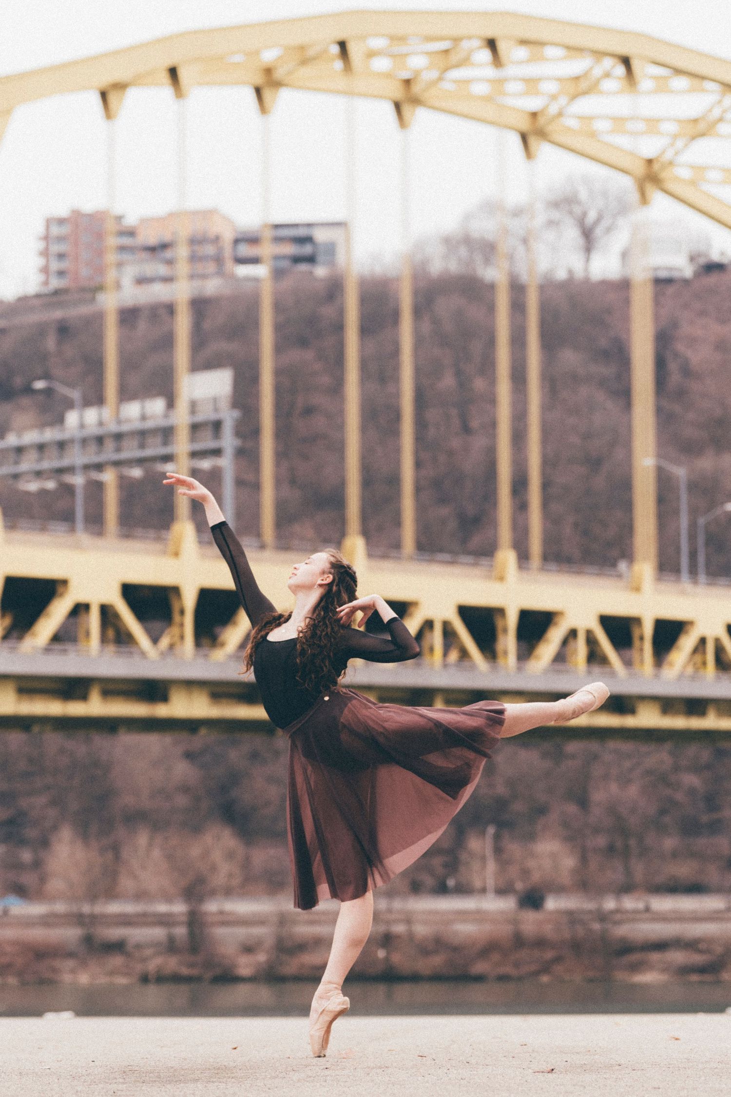 Ballerina performing an arabasque with Fort Pitt Bridge and golden sky in the background at Point State Park pittsburgh dance photography