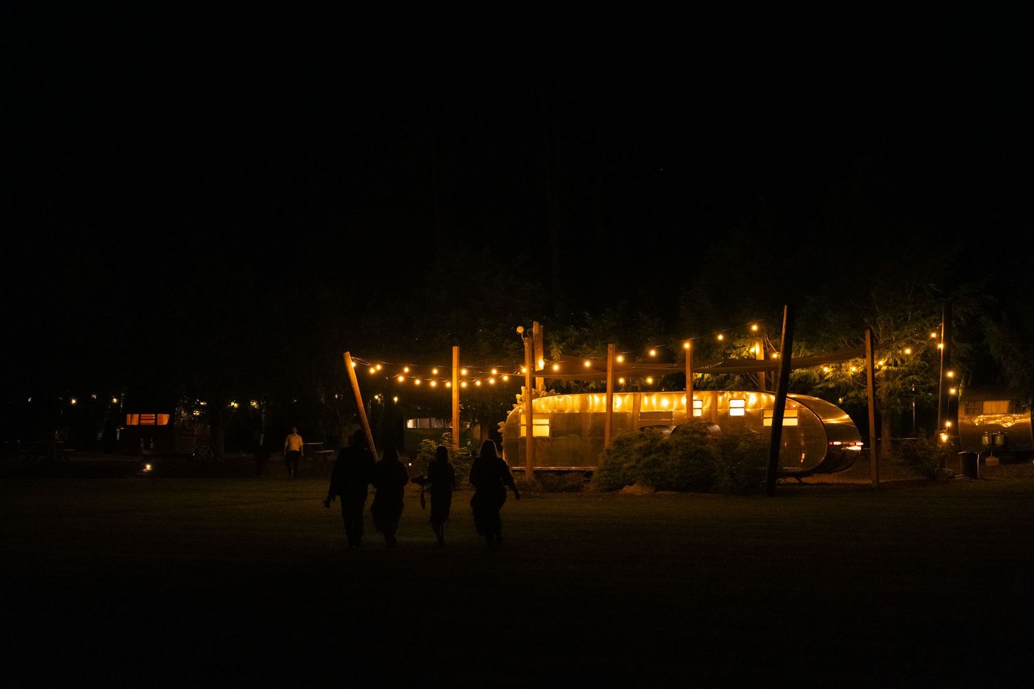 Silhouettes of people walking at night with glowing lights from buildings in the distance creating an atmospheric scene.