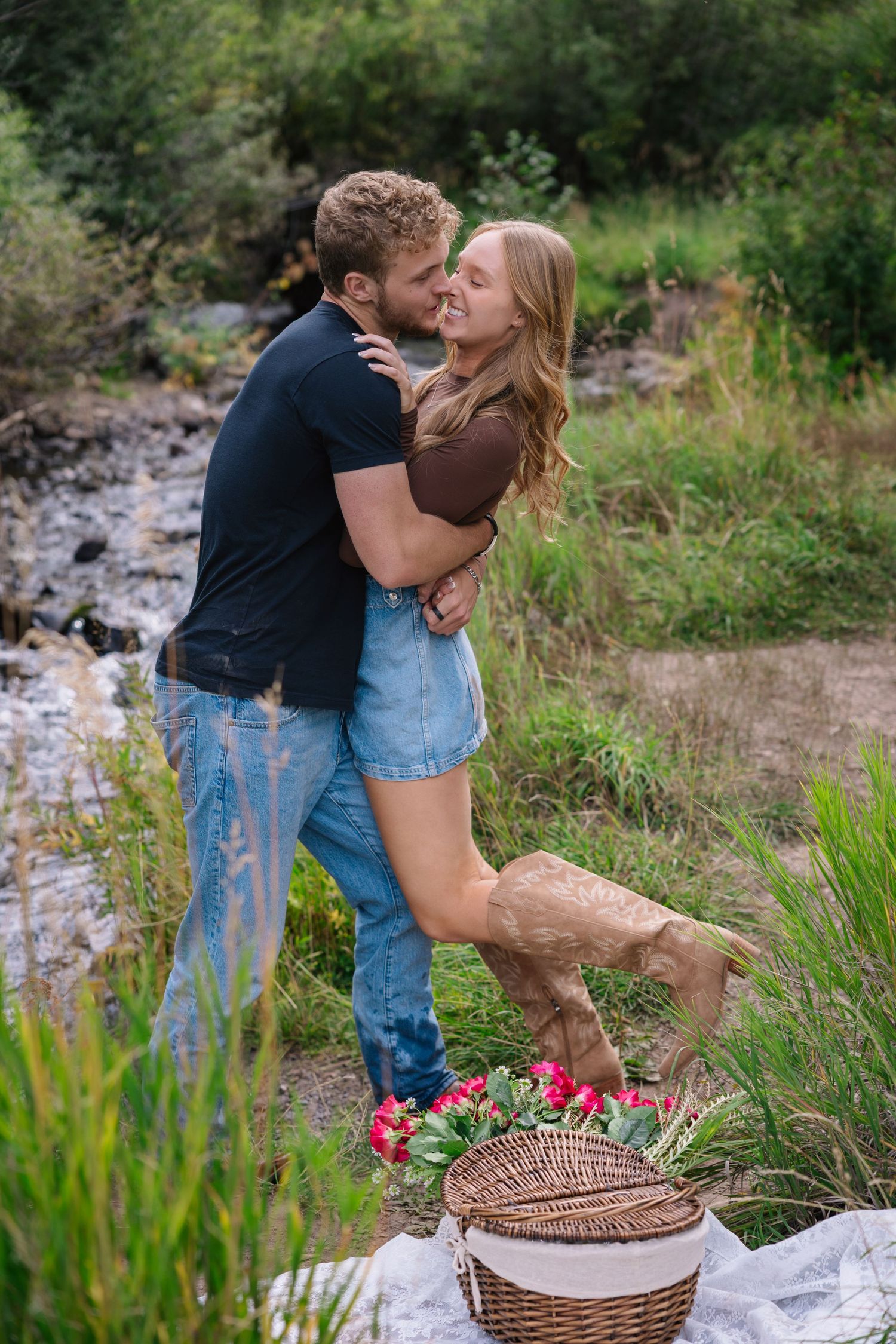 A romantic outdoor picnic scene unfolds with a couple embracing near a woven basket in a grassy meadow setting. Knoxville Photographer