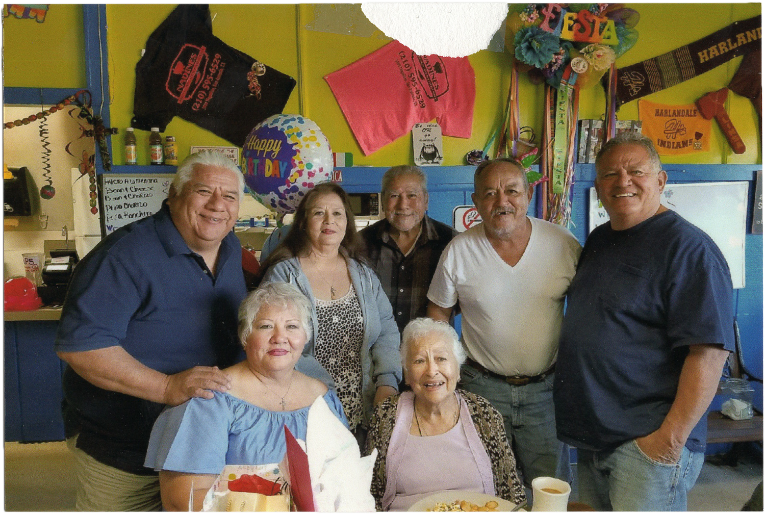Group of people gathered together smiling inside a casual dining establishment with colorful decorations on the walls.
