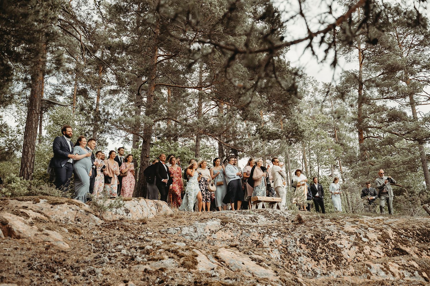 Bröllopsgäster på utomhusvigsel på en klippa vid skogen i Vrena, Nyköping. Bröllopsfotograf Josefin Landhagen, Lets Bloom Media.