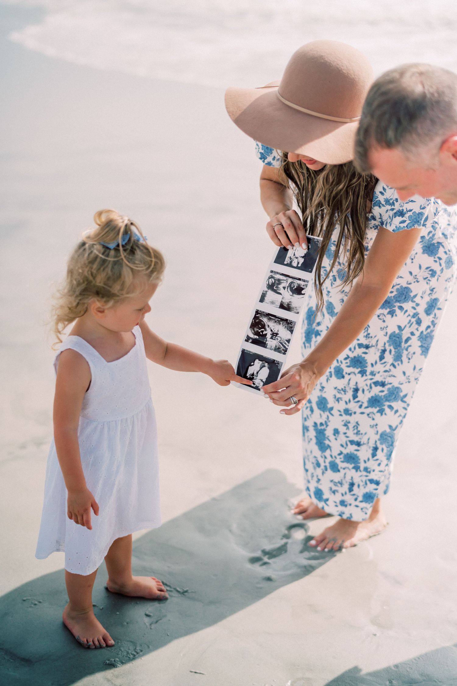 A couple shares a tender moment on a wooden boardwalk at the beach, with the woman wearing a blue floral maternity dress.
