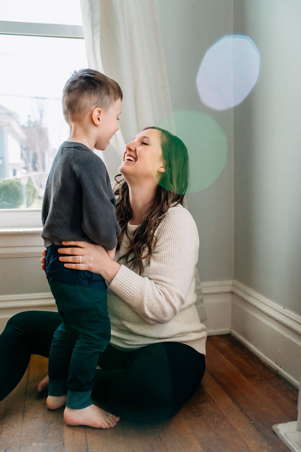 A tender moment between parent and child on hardwood floors shows playful interaction in natural light in Grand Rapids
