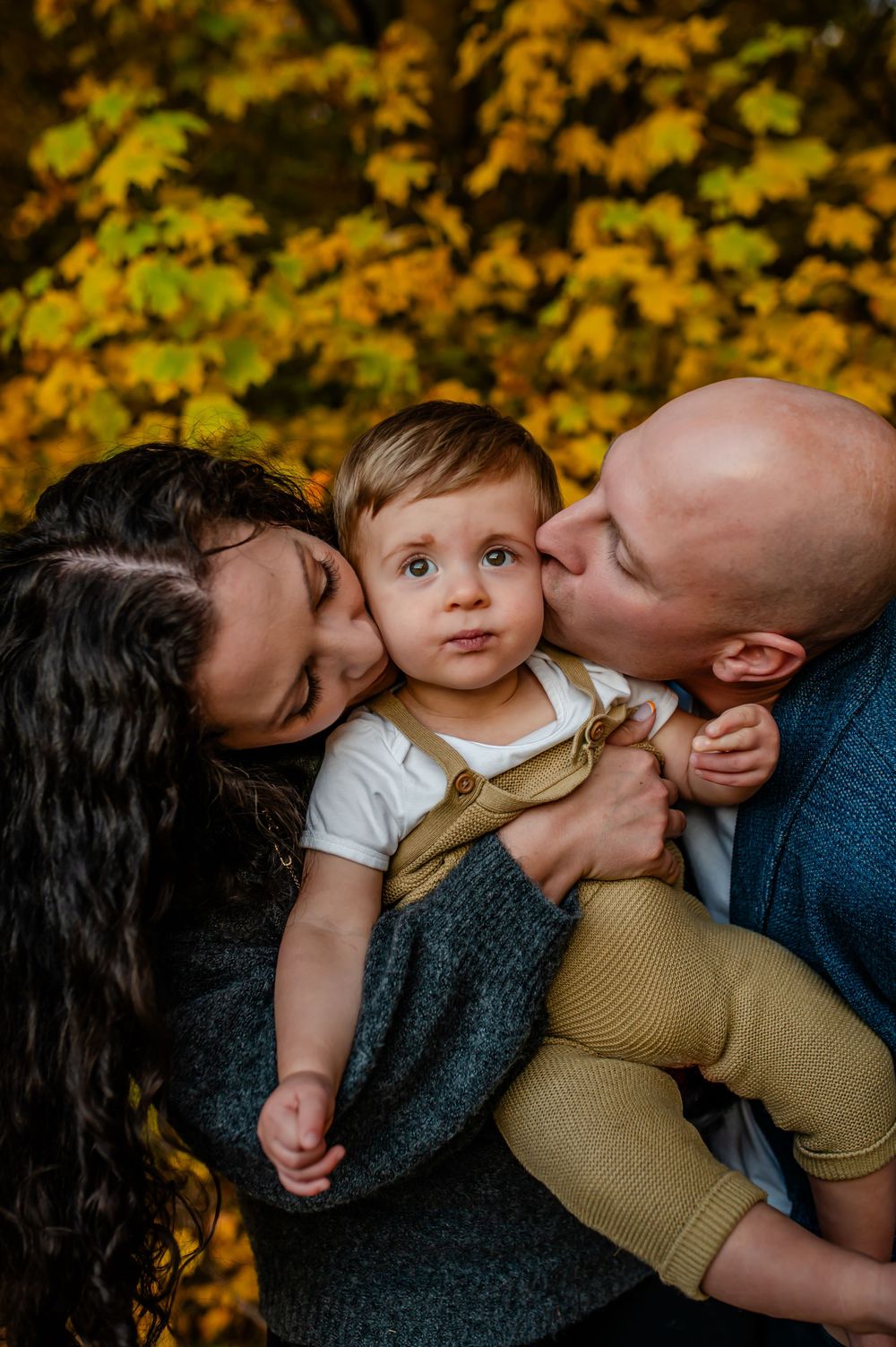 Family shares tender moment outdoors against backdrop of golden autumn foliage in touching portrait.