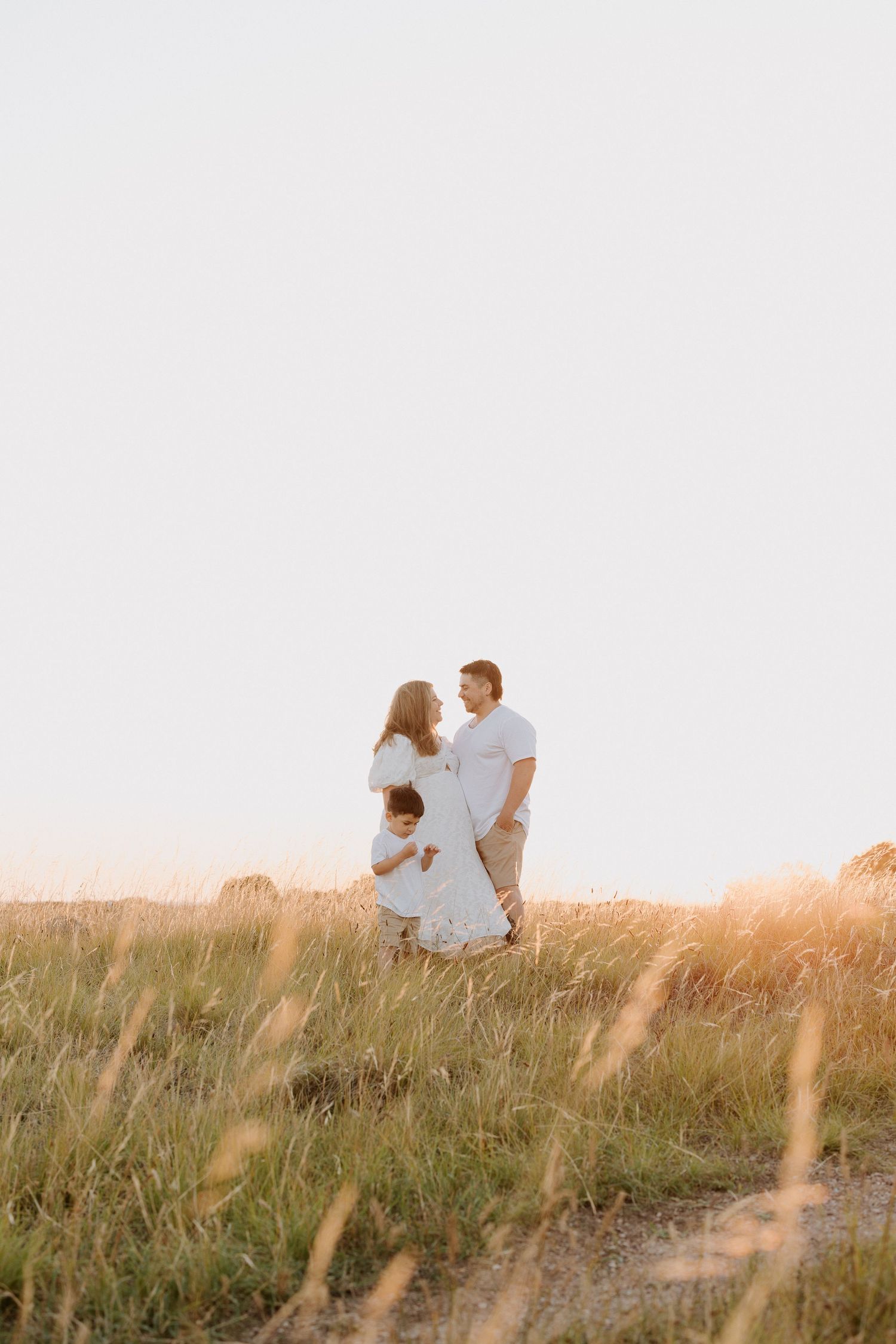 A family shares an intimate moment together in a sun-lit field of tall grass.