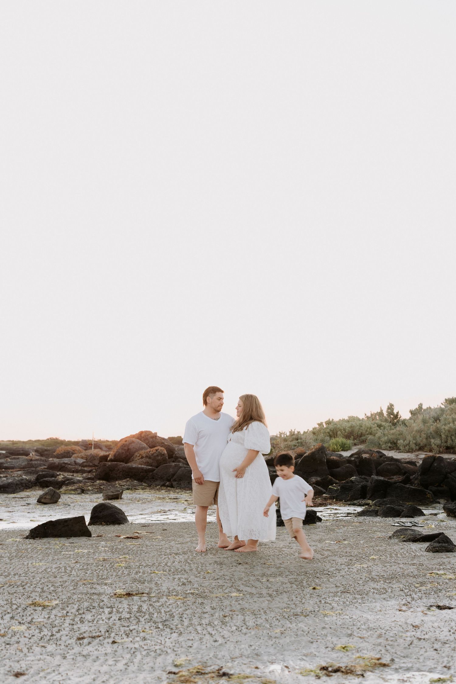 A family stands together on rocky beach terrain during golden hour.