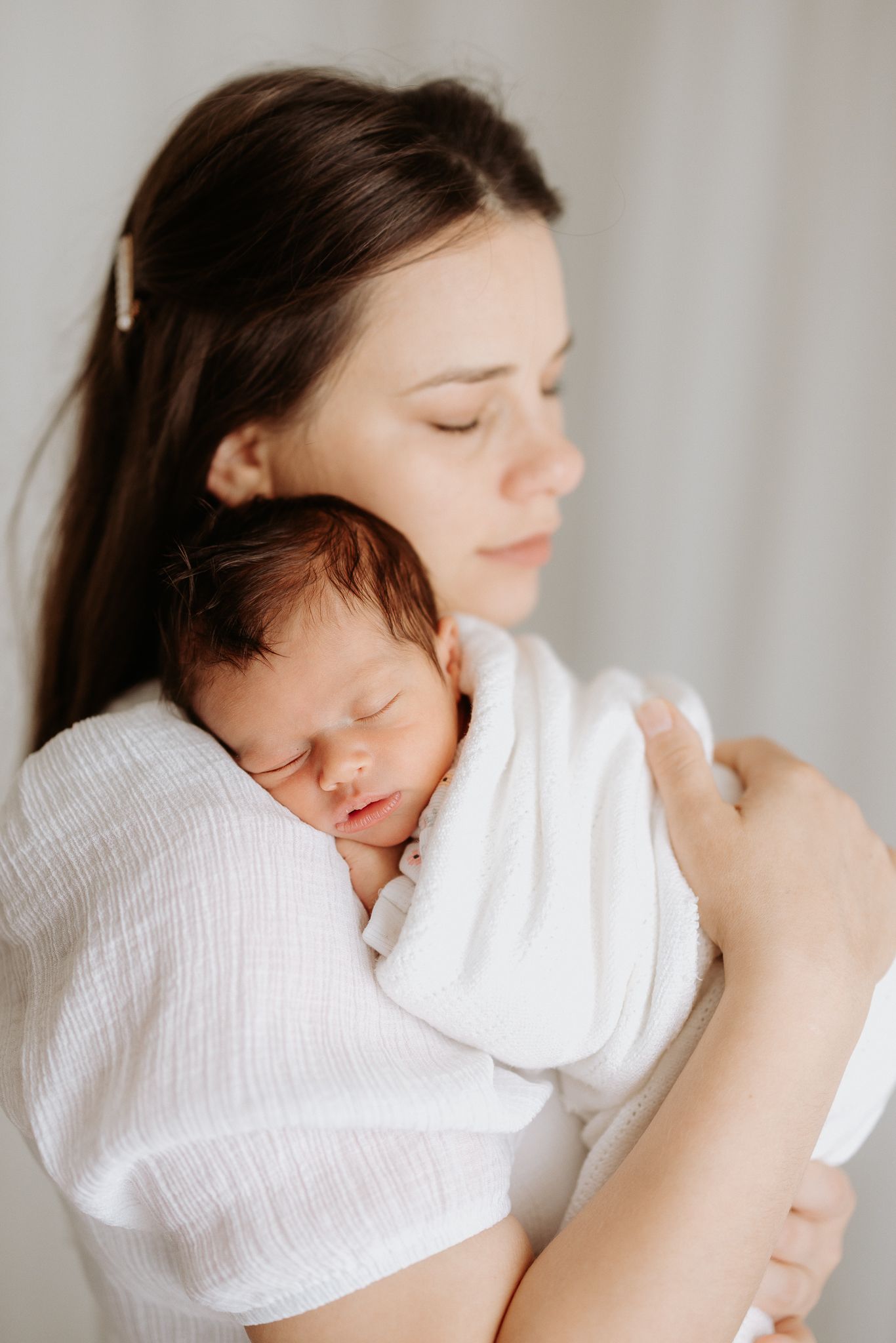 Peaceful moment with sleeping newborn wrapped in white blanket.