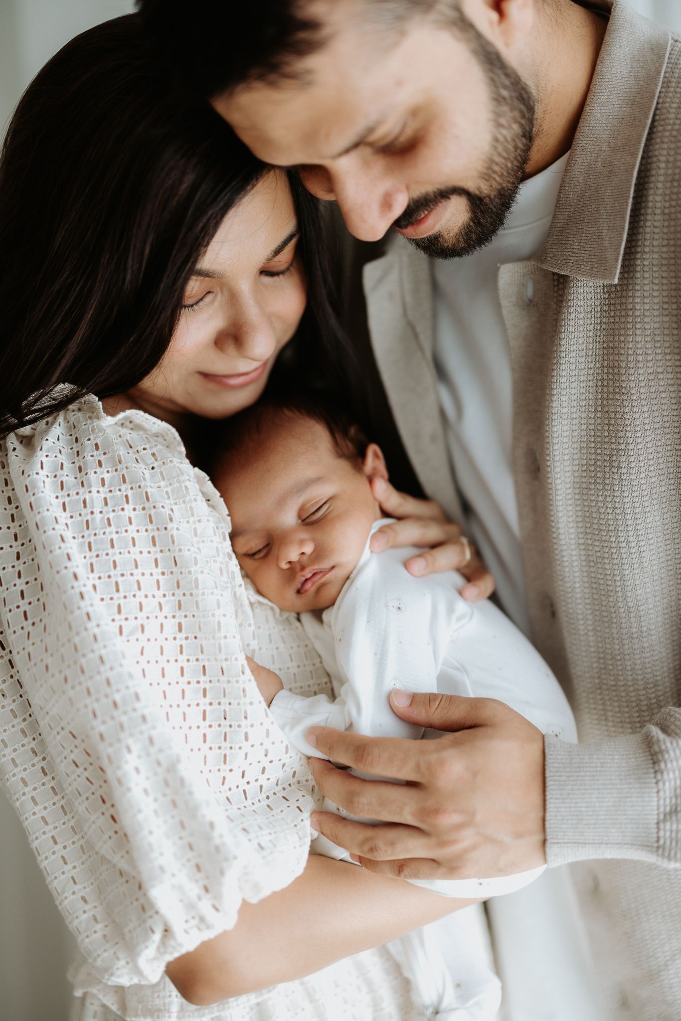 Tender family moment with newborn baby in white attire.