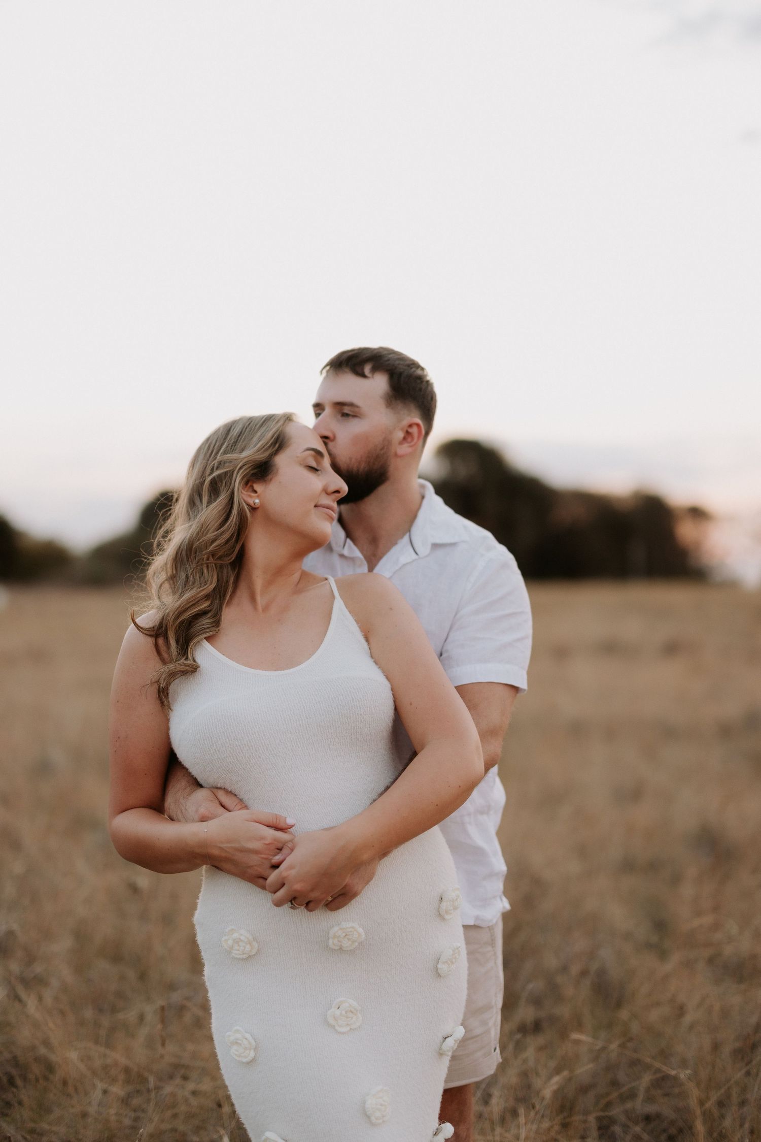 Romantic couple shares intimate moment in field during golden hour sunset.