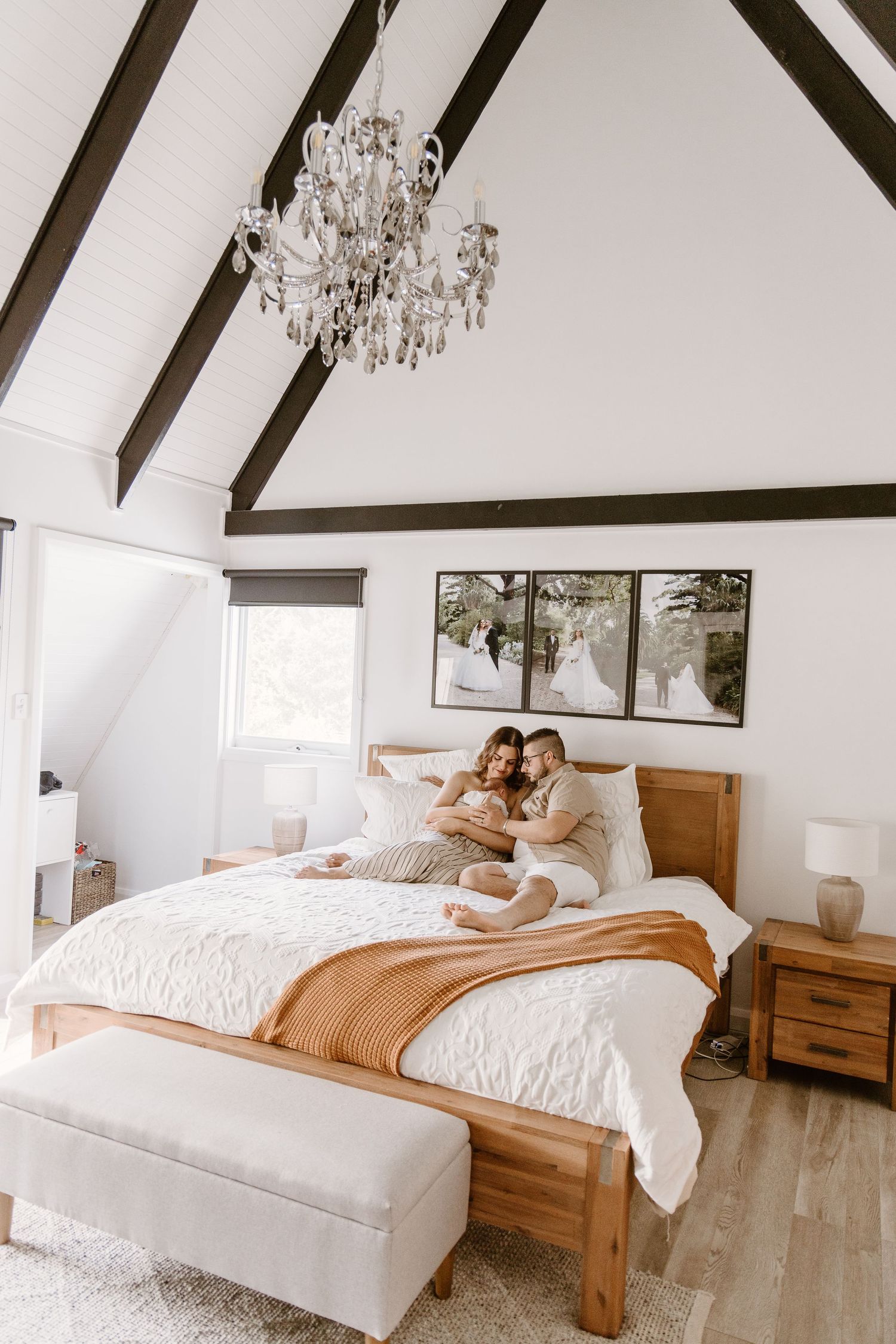Cozy bedroom interior with vaulted ceiling, crystal chandelier, wooden bed frame and white bedding.