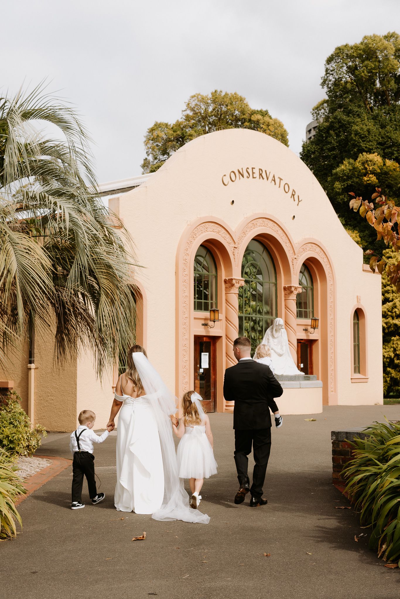 Wedding party enters pink conservatory building with flower girls and ring bearer.