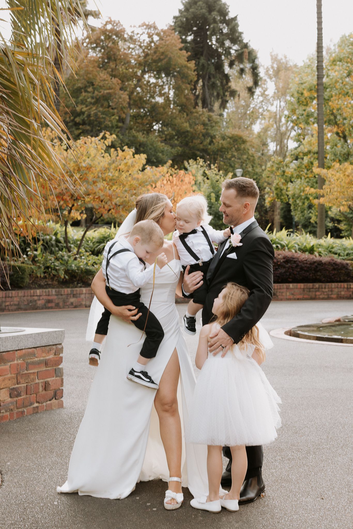 Wedding couple shares joyful moment with children in formal attire outside.