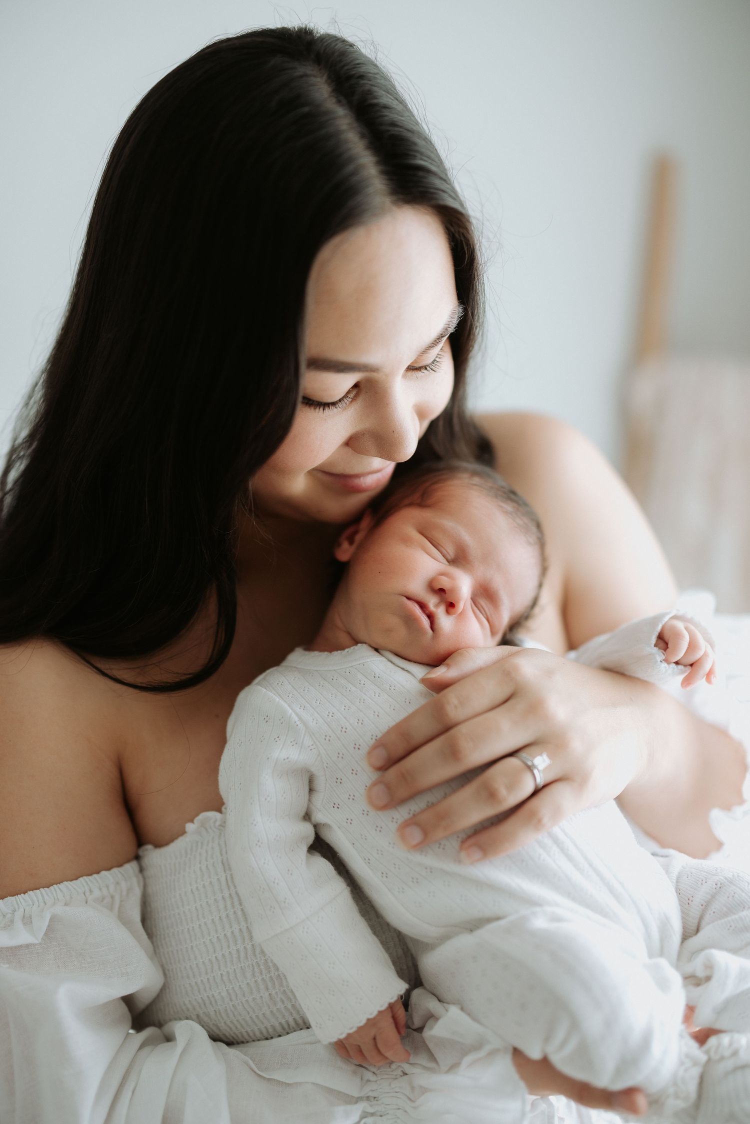 Intimate portrait of mother and newborn baby sharing tender moment in white clothing.