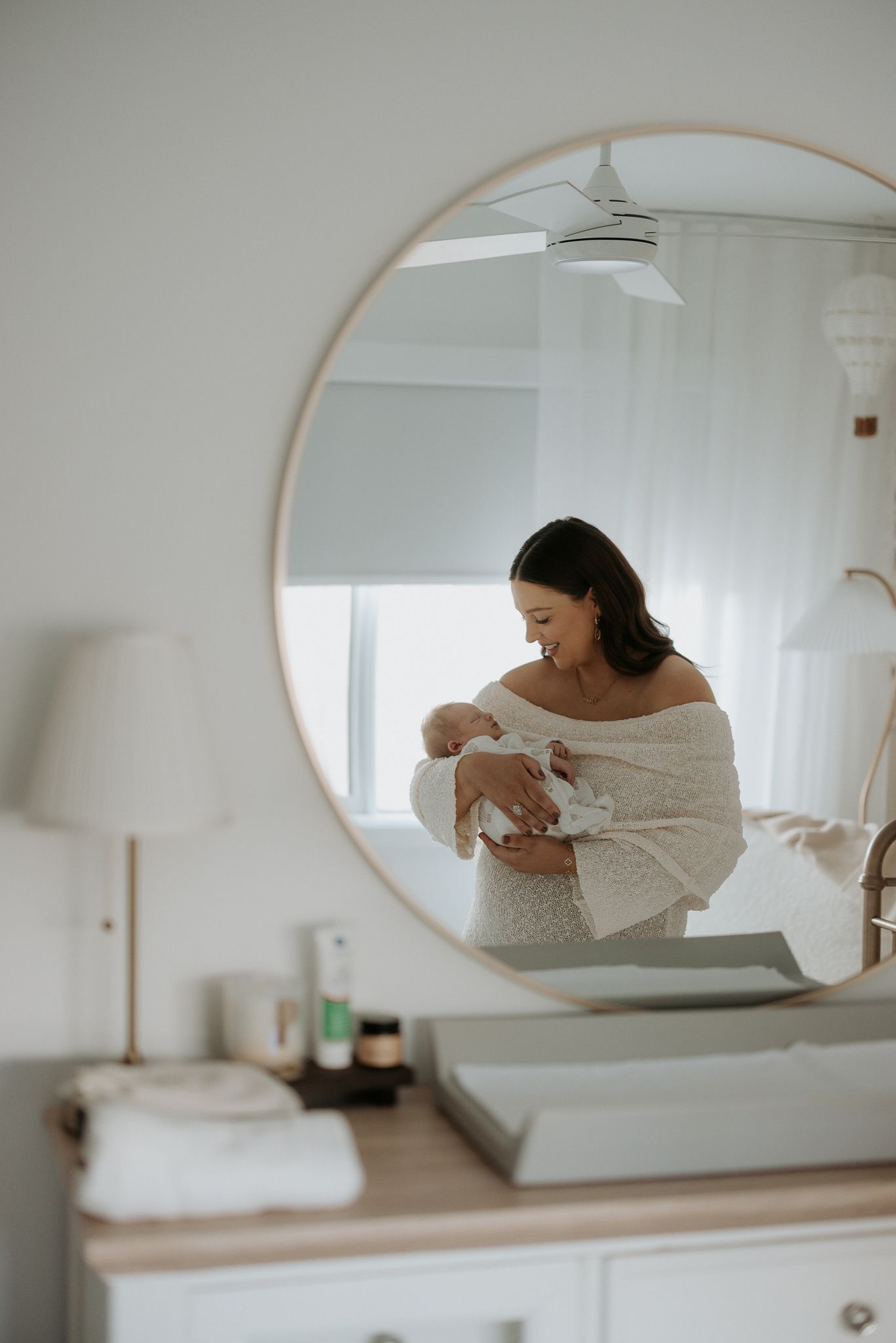 Mirror reflection of parent holding baby in white modern bedroom.
