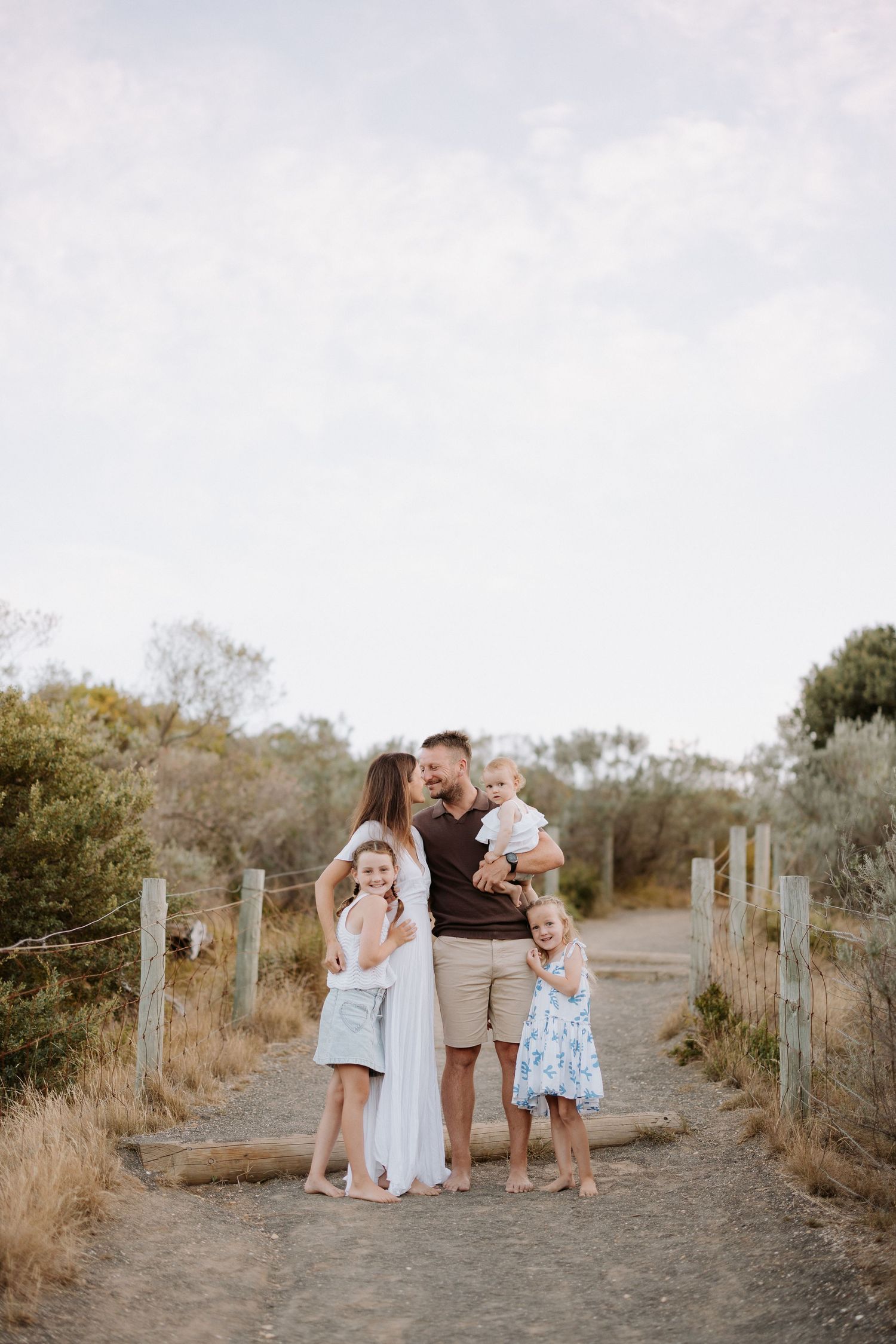 A family poses together on a dirt path surrounded by dry brush and fencing.