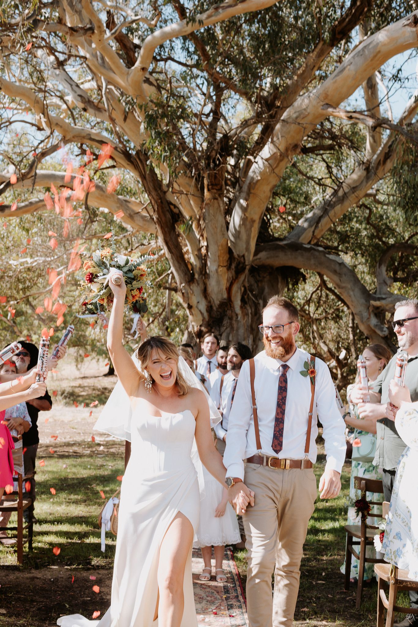Newlyweds celebrate joyfully under a large eucalyptus tree during an outdoor rustic wedding ceremony.