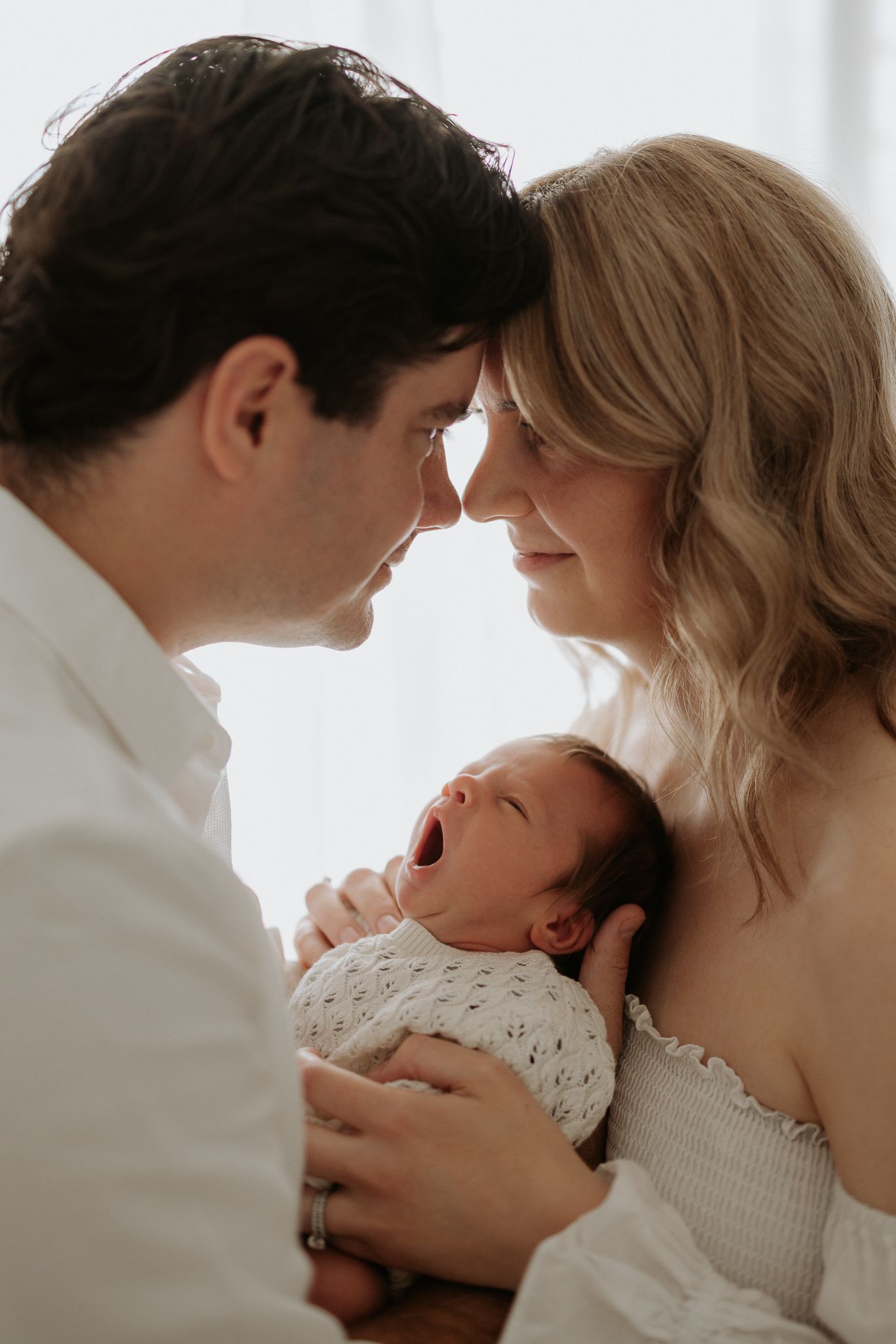 Intimate family moment with newborn baby in white setting.