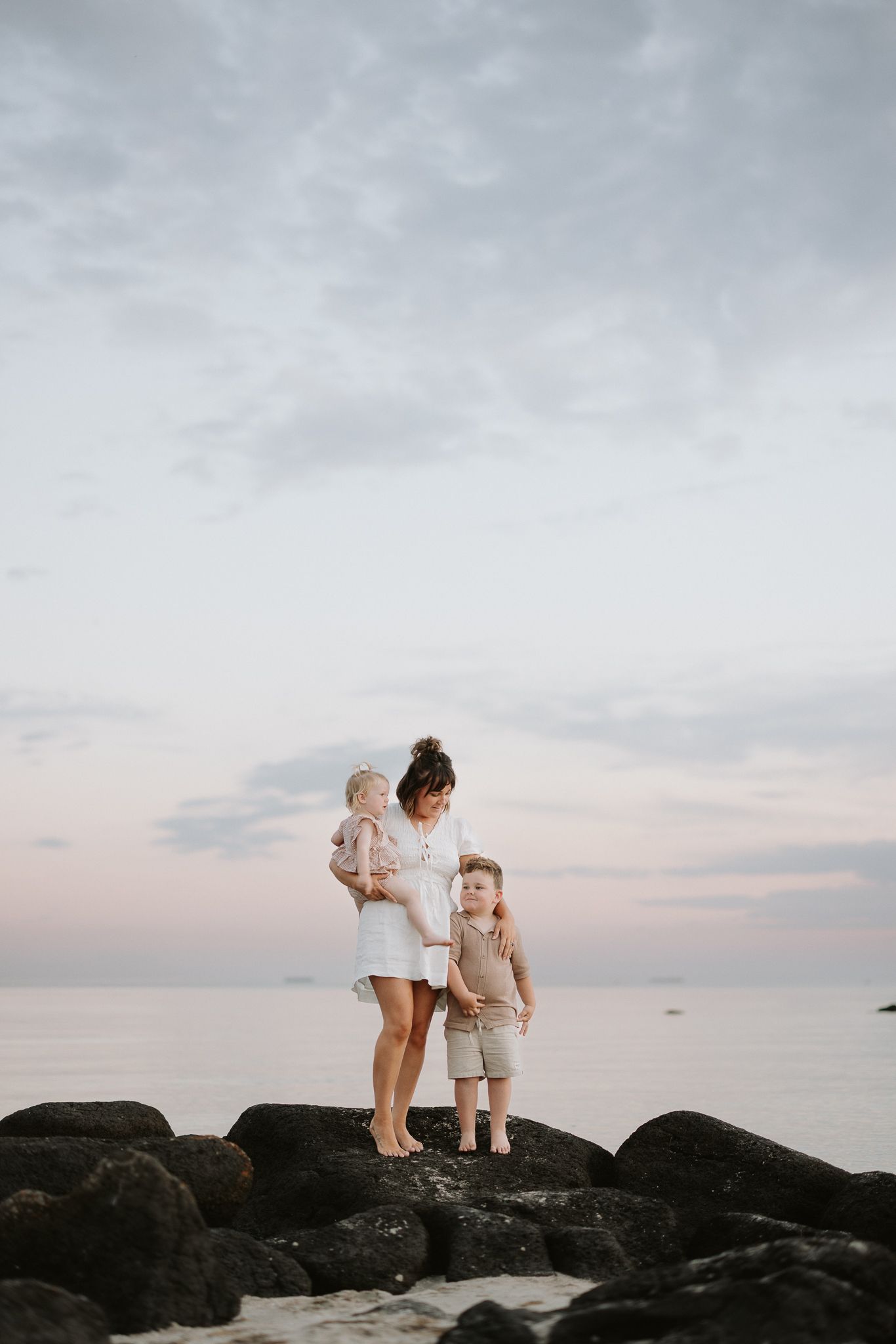 Family standing on rocky coastline at sunset.