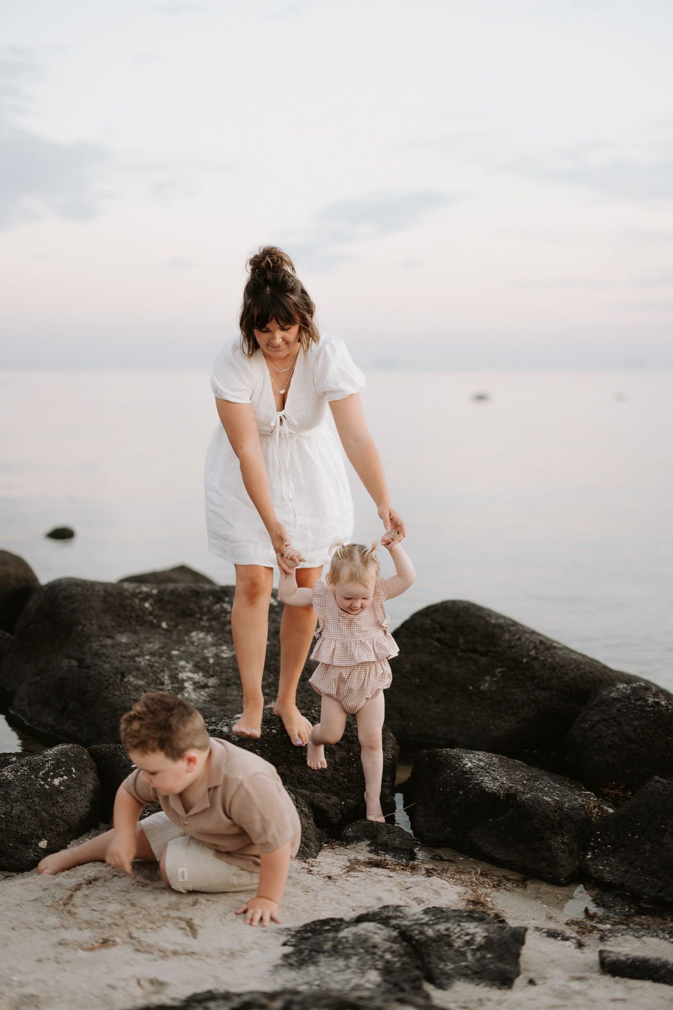 Family exploring rocky beach together at dusk.